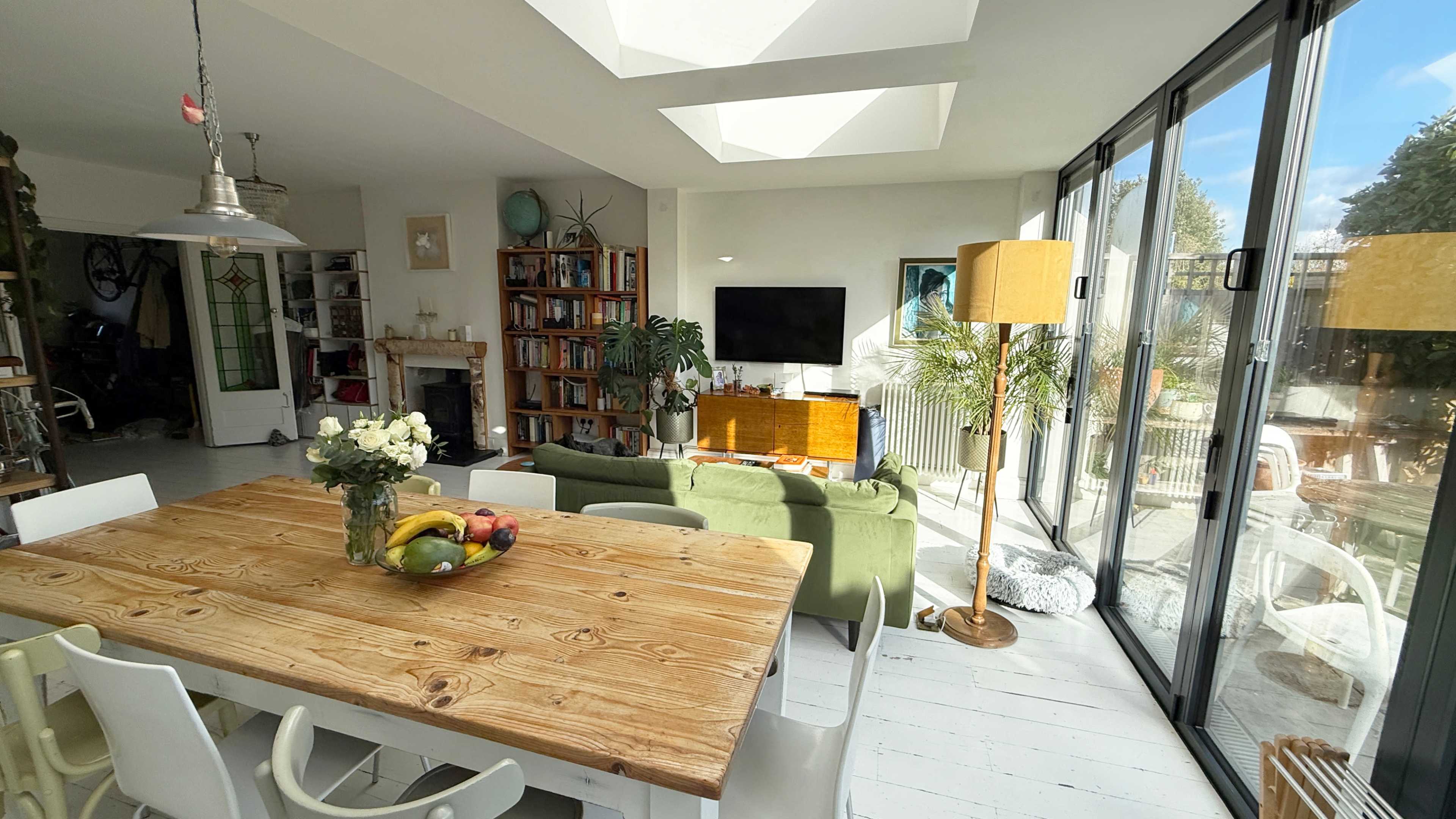A wooden dining table with chairs is set in a bright, open space featuring large windows and a cozy seating area.