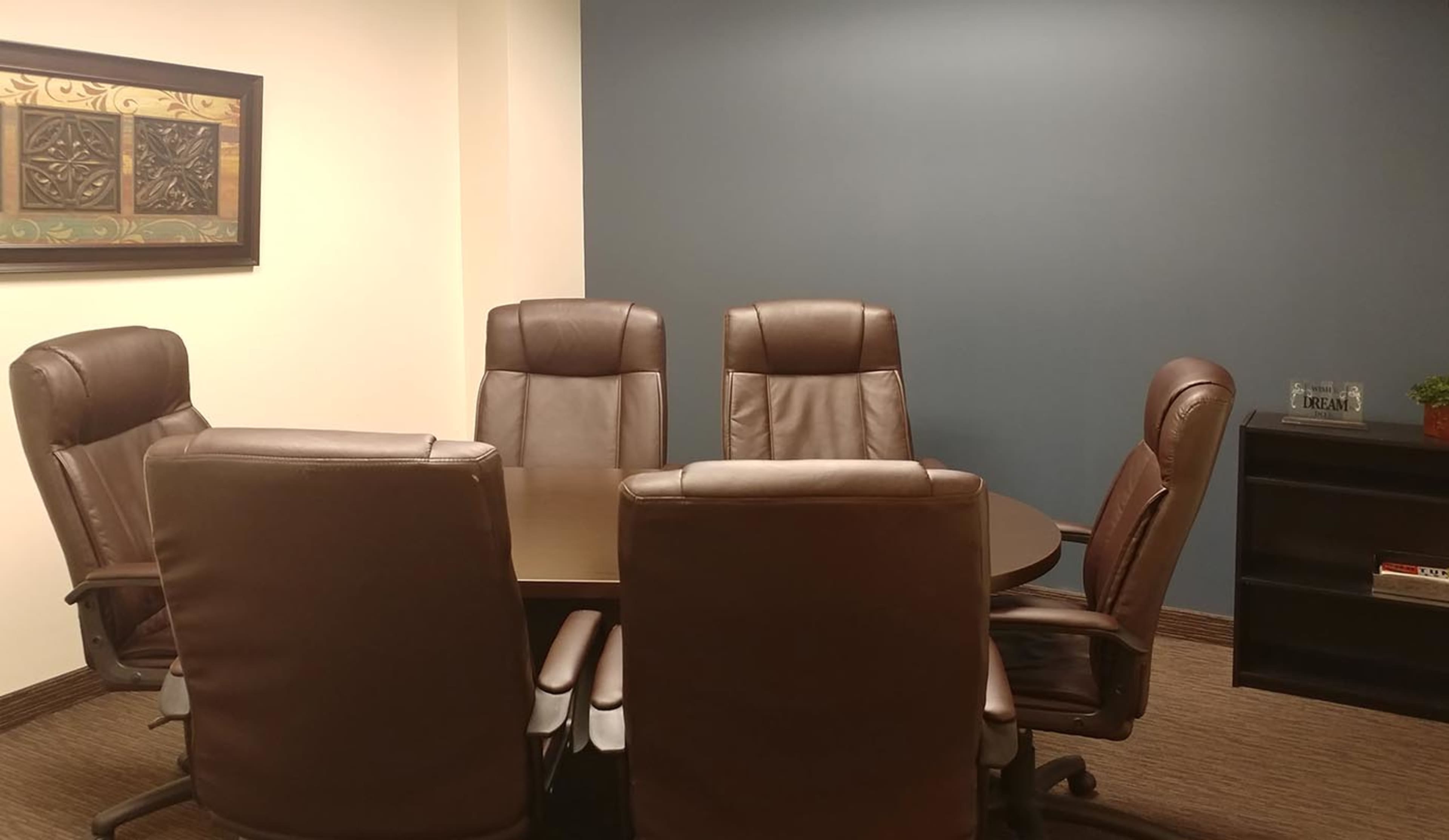 A conference room features a circular table surrounded by five leather office chairs and a dark blue wall.