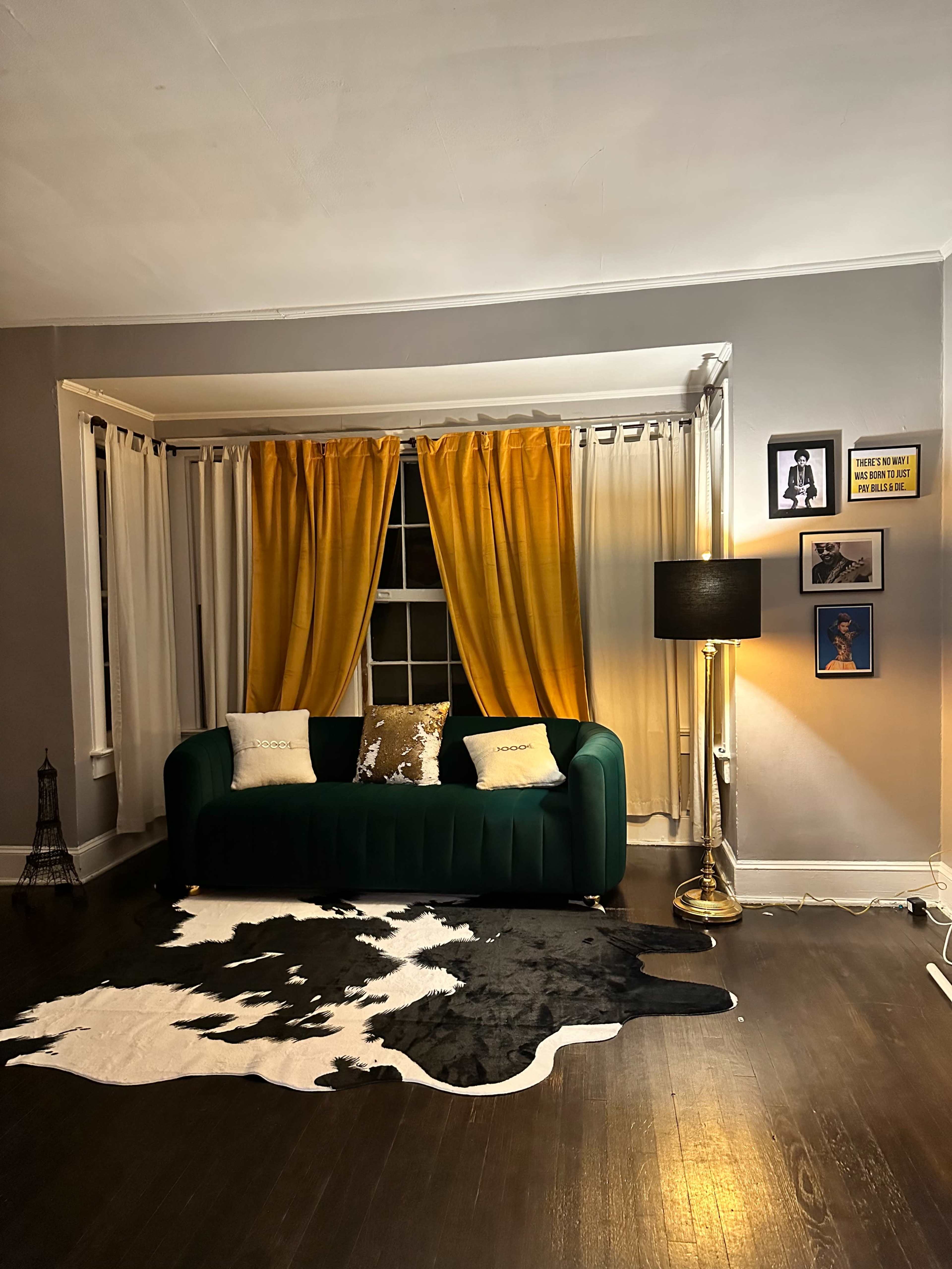 A stylish living room featuring a green couch, yellow curtains, a black floor lamp, and a cowhide rug.