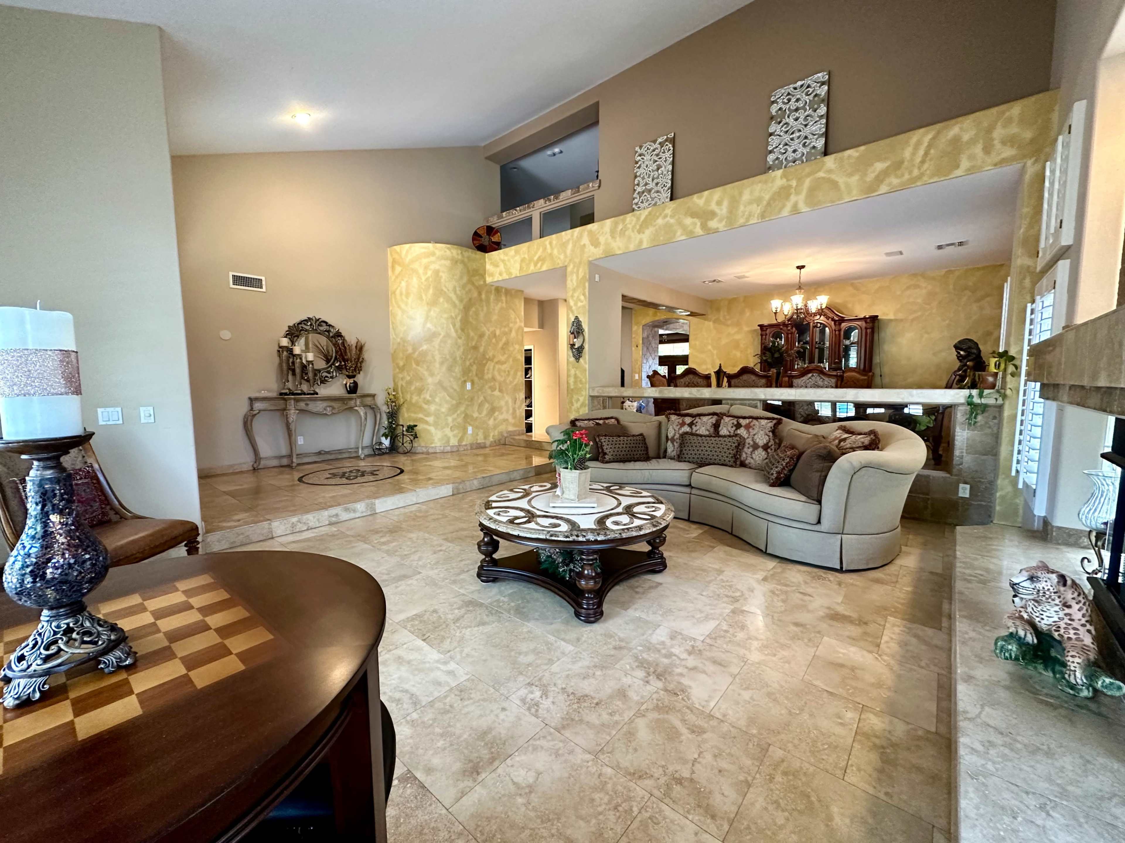 A spacious living area features a beige sectional couch, a decorative table, and marble flooring with warm-colored walls.
