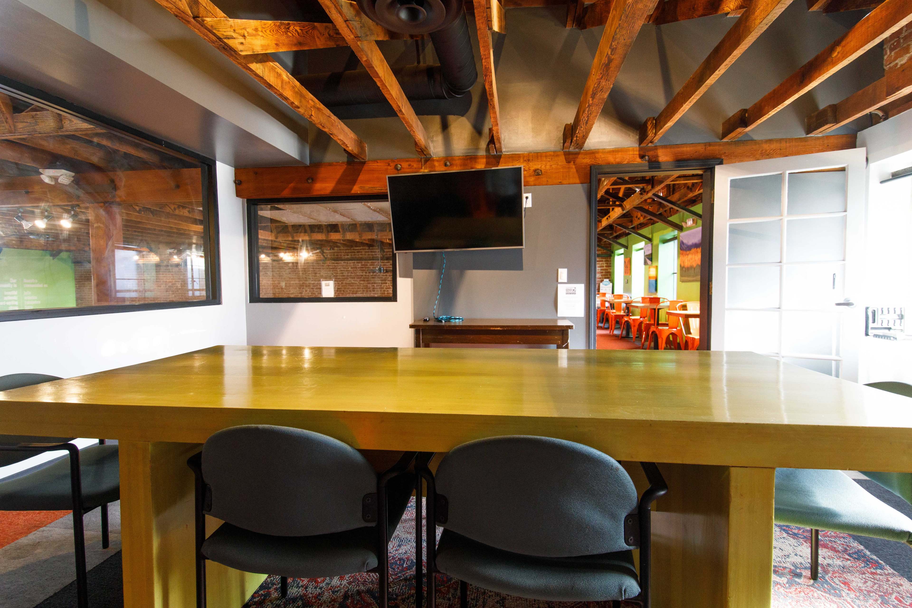 A meeting room features a large wooden table, several chairs, and a wall-mounted television.