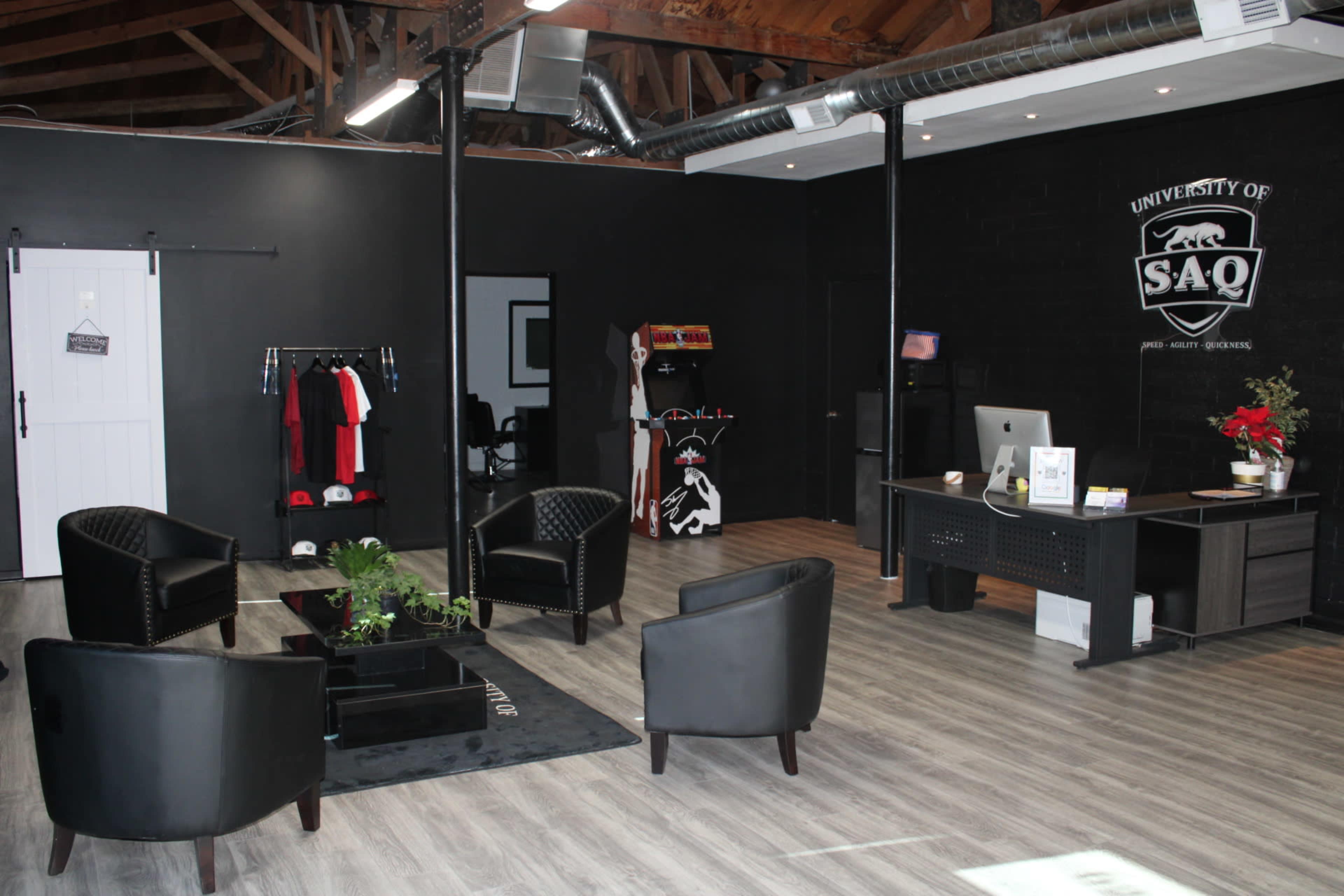 An office space featuring a black wall, modern furniture, a desk with a computer, and a small seating area with four chairs arranged around a central plant.