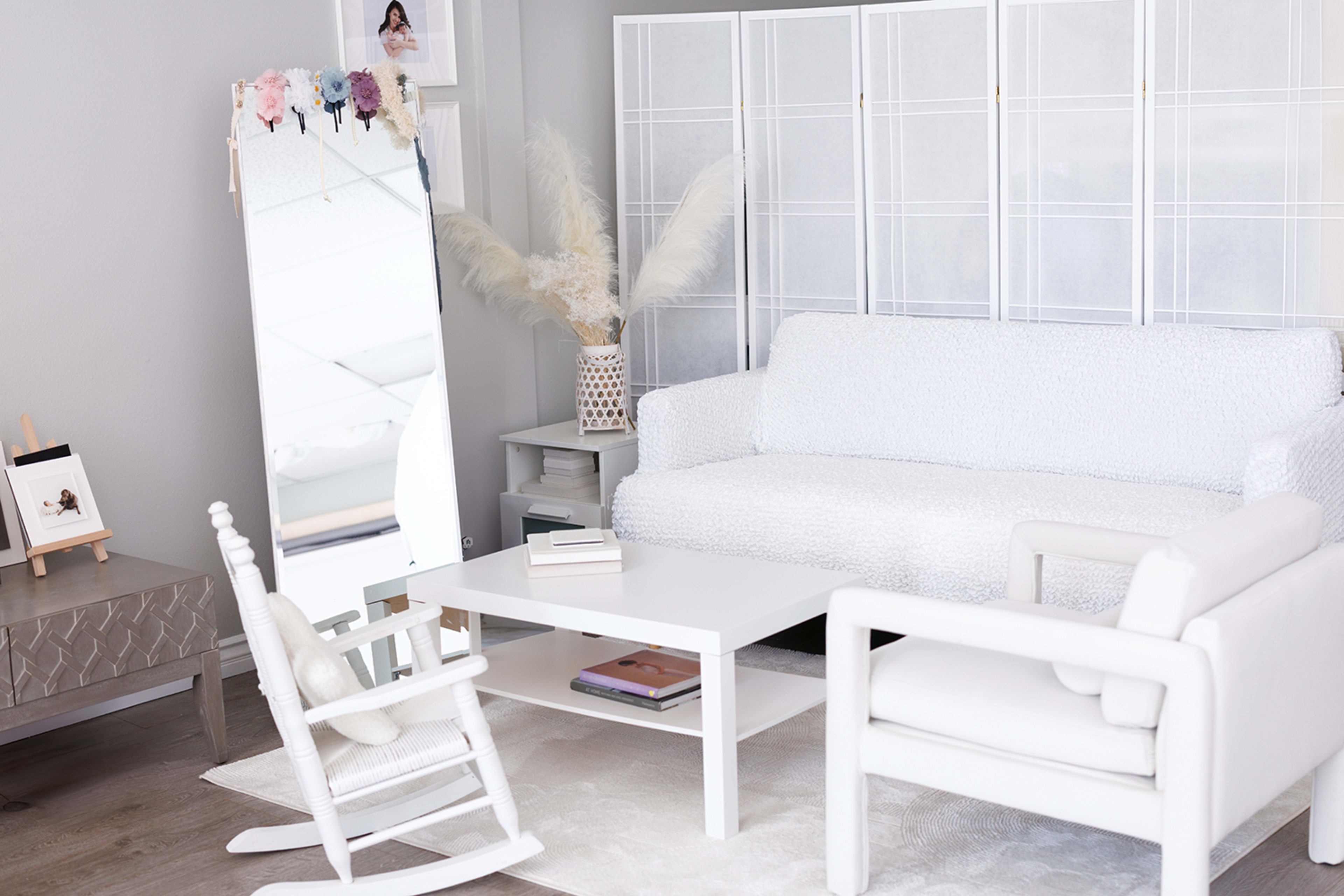 The image shows a bright, modern living room featuring a white sofa, a mirror, and a rocking chair arranged around a simple coffee table.