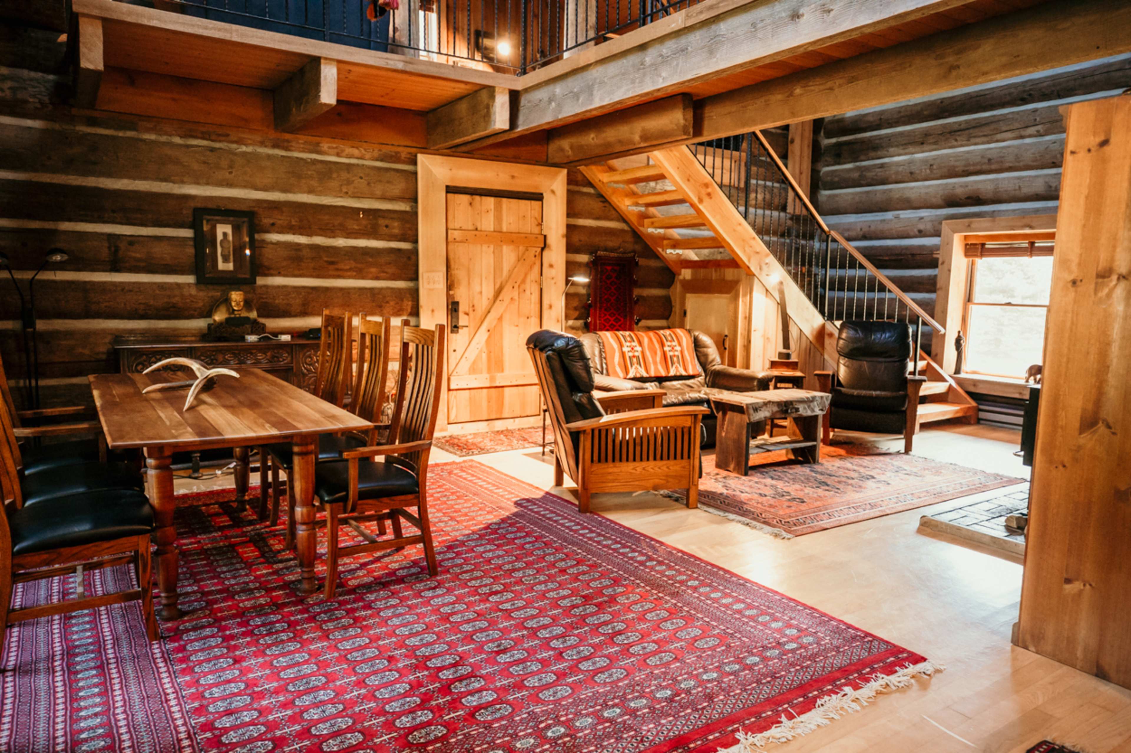 A cozy log cabin interior with wooden furniture, a dining table, and a staircase.