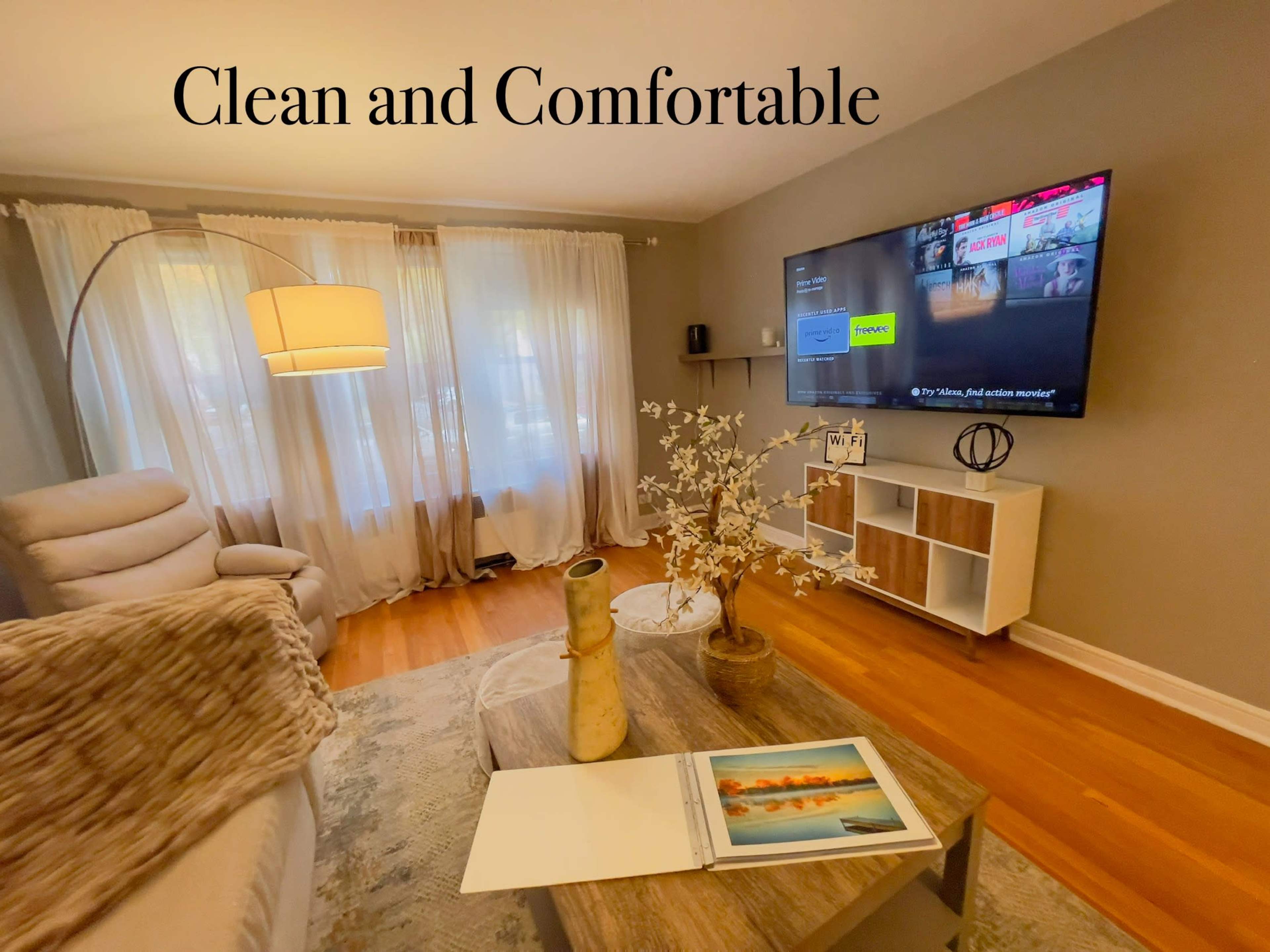 A living room features a light-colored sofa, a modern television mounted on the wall, and a coffee table with decor items.