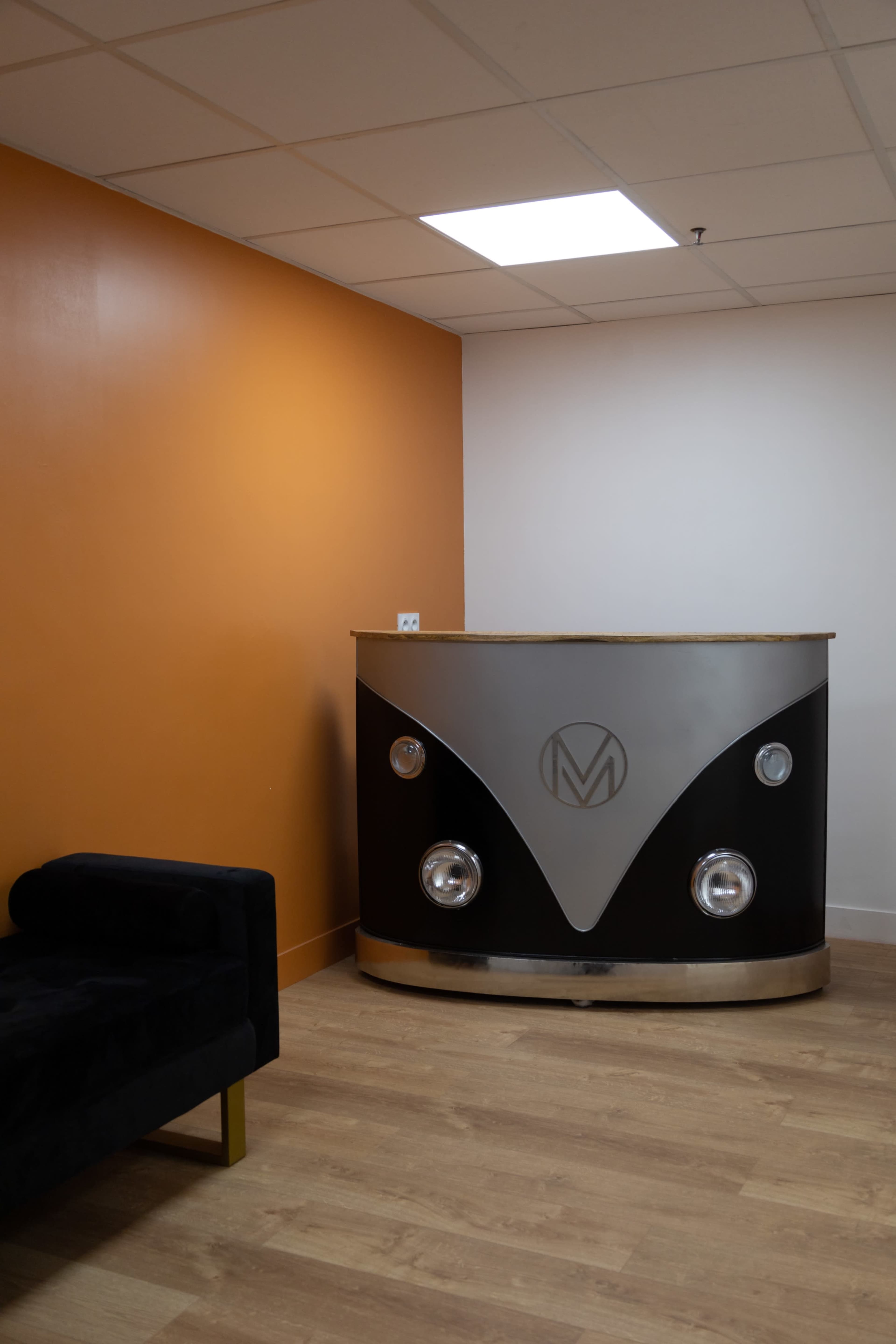 A modern reception desk with a logo on it, positioned against an orange wall in a well-lit room.