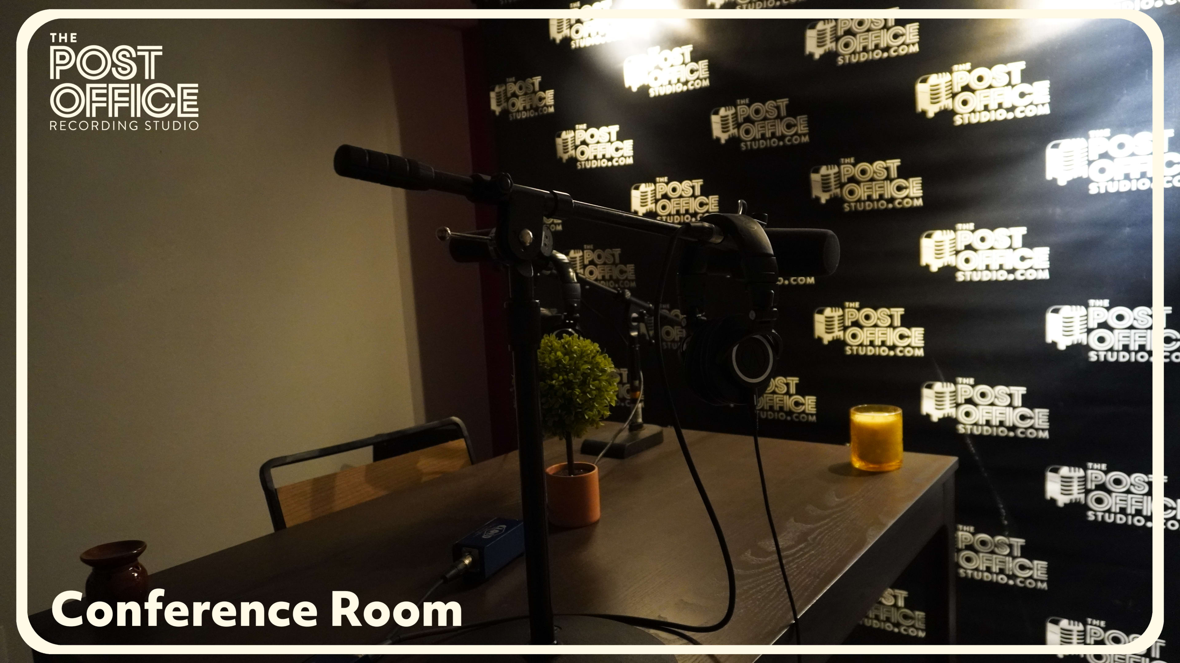 The image shows a conference room equipped with a microphone and a small plant on a table, against a backdrop featuring the logo of The Post Office Recording Studio.