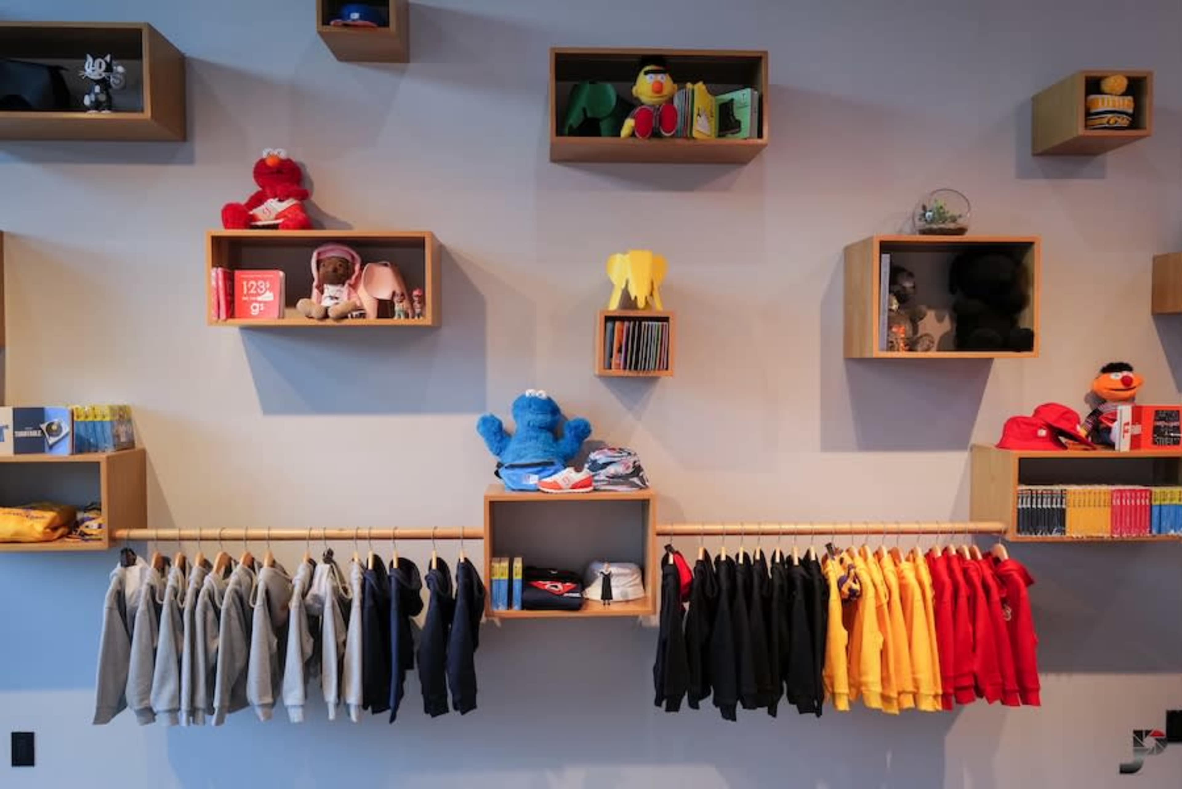 A display wall in a retail store with shelves holding plush toys and clothing items, including sweatshirts in various colors hanging below.