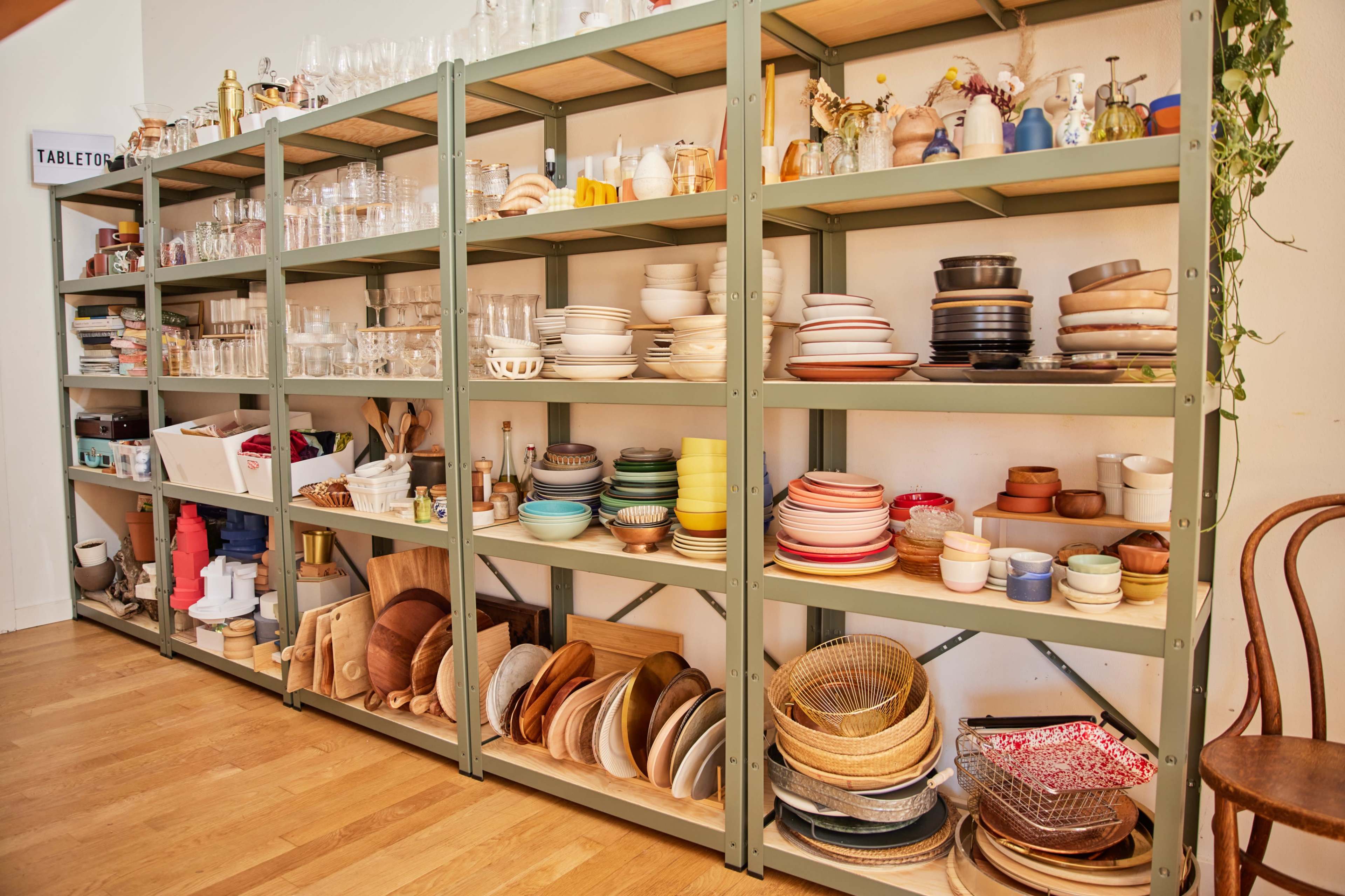 A set of metal shelving units displays an array of glassware, dishware, and kitchen tools organized neatly by type and color.