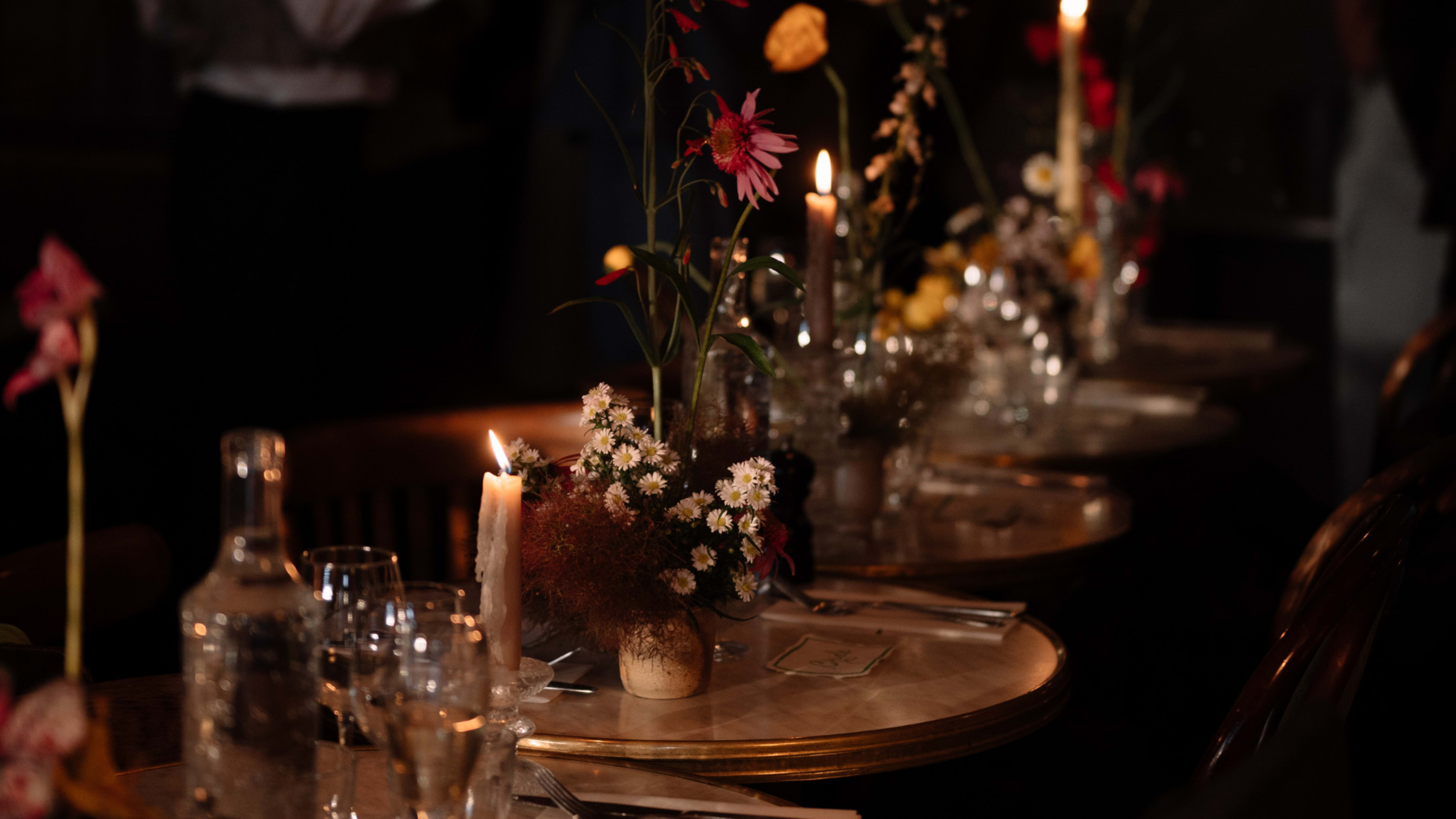 A dining table set with candles, floral centerpieces, and glassware in a dimly lit setting.