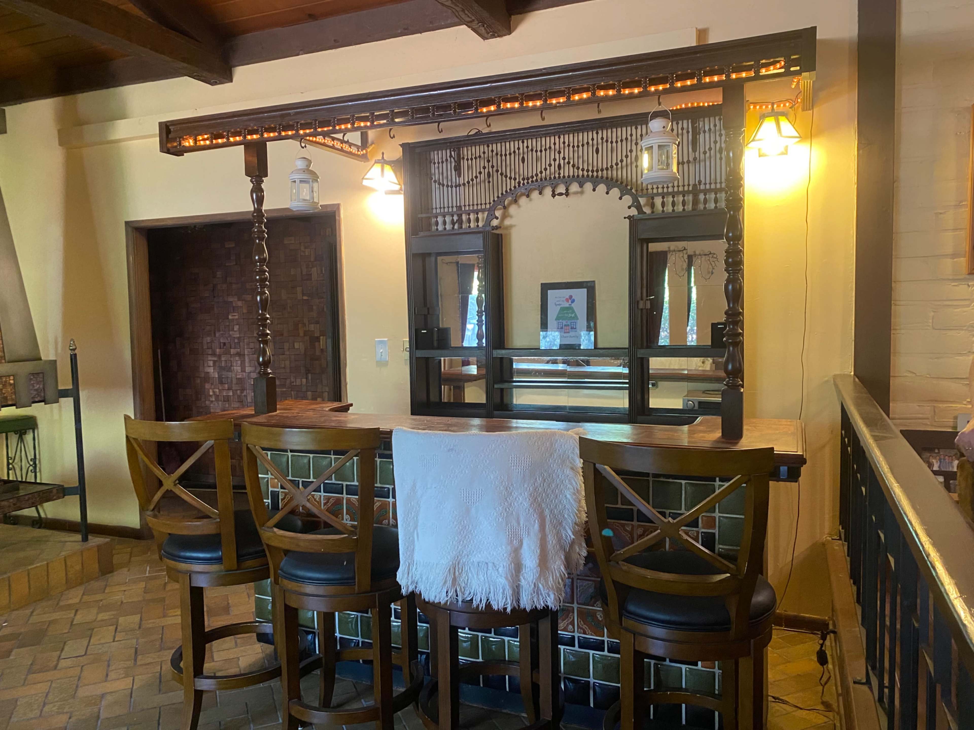 A wooden bar area with high-backed stools in a warmly lit room featuring a decorative mirror and lighting fixtures.