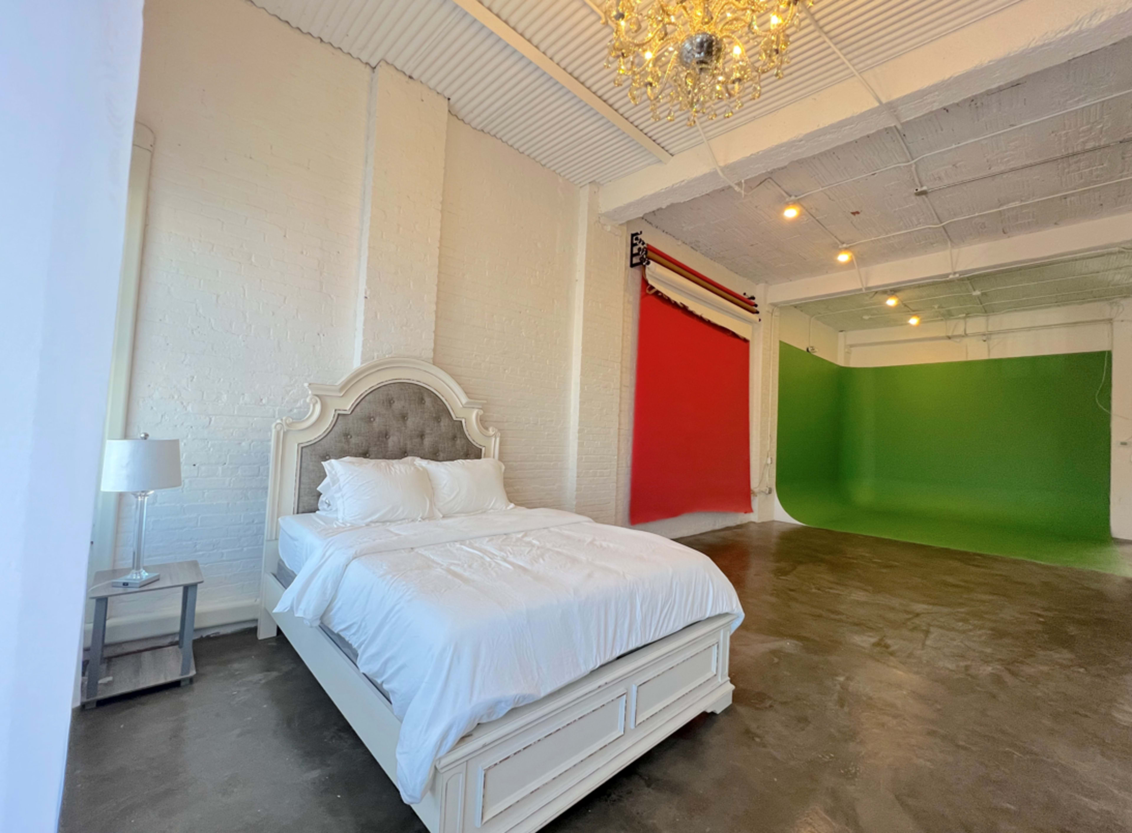 A bright bedroom features a white bed with plush bedding and a backdrop of red and green walls in the background.