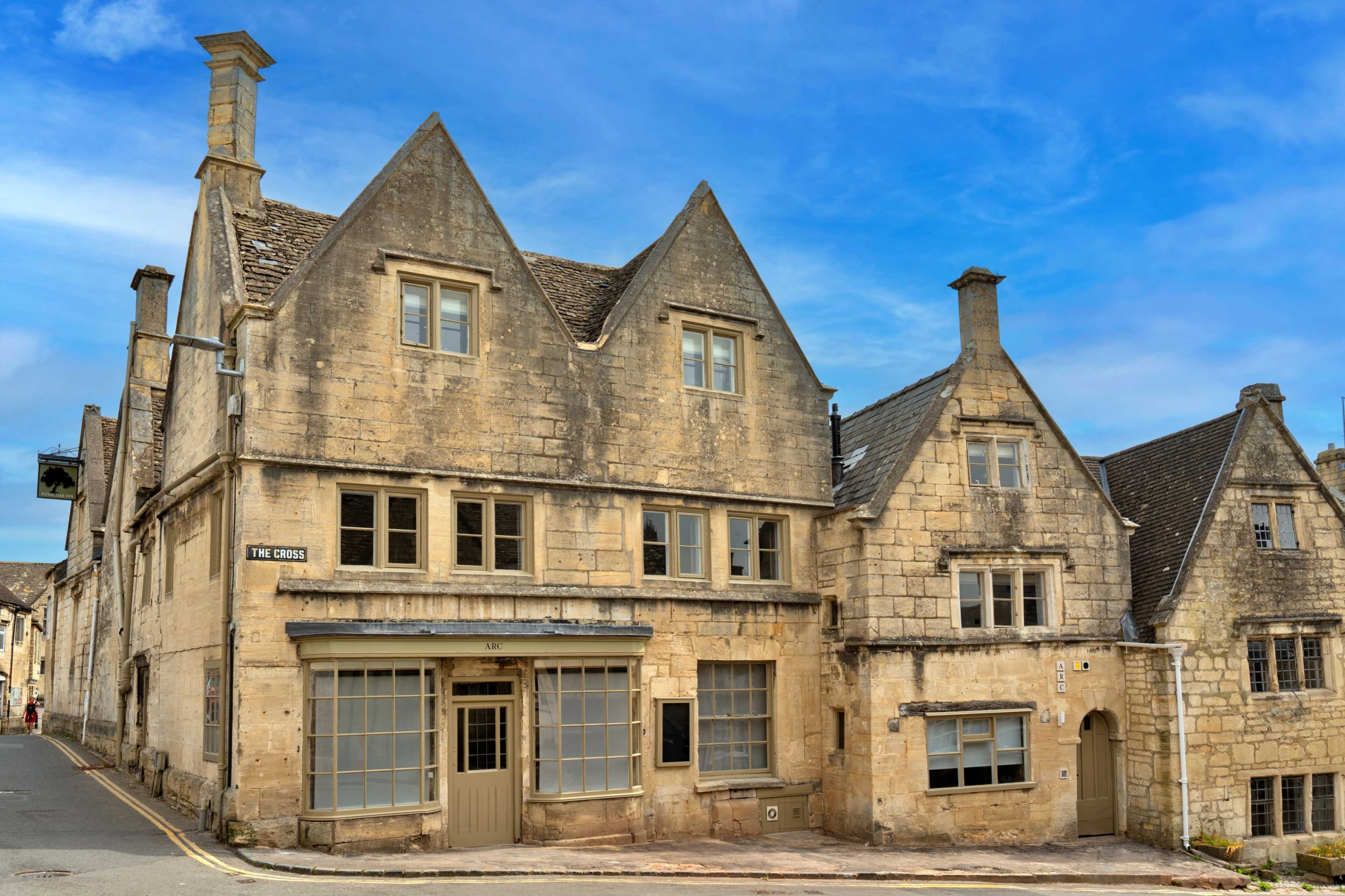 Two stone buildings with steep roofs, situated on a quiet street under a blue sky.