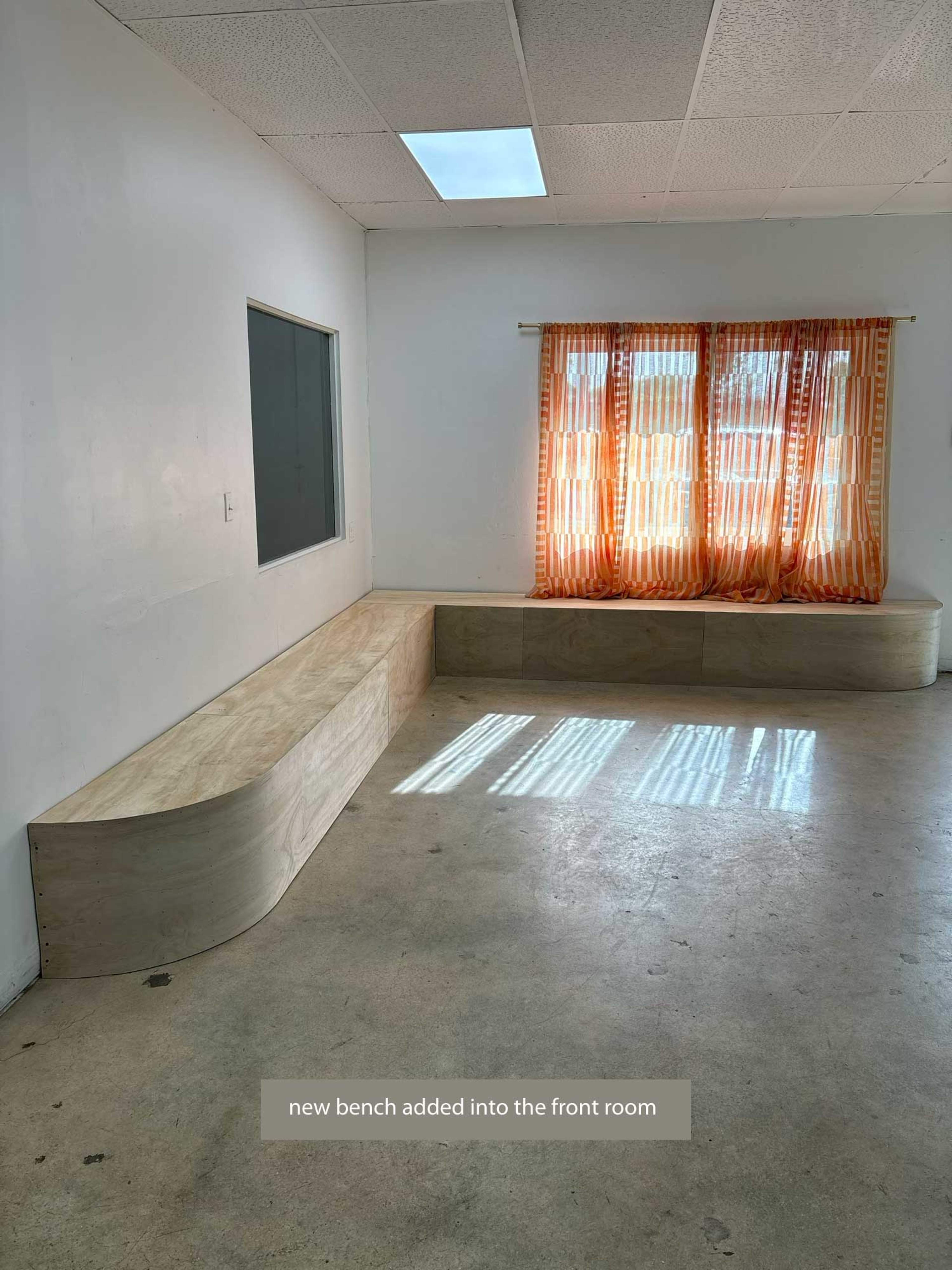 A new wooden bench is installed in the front room, adjacent to a window with orange-striped curtains.