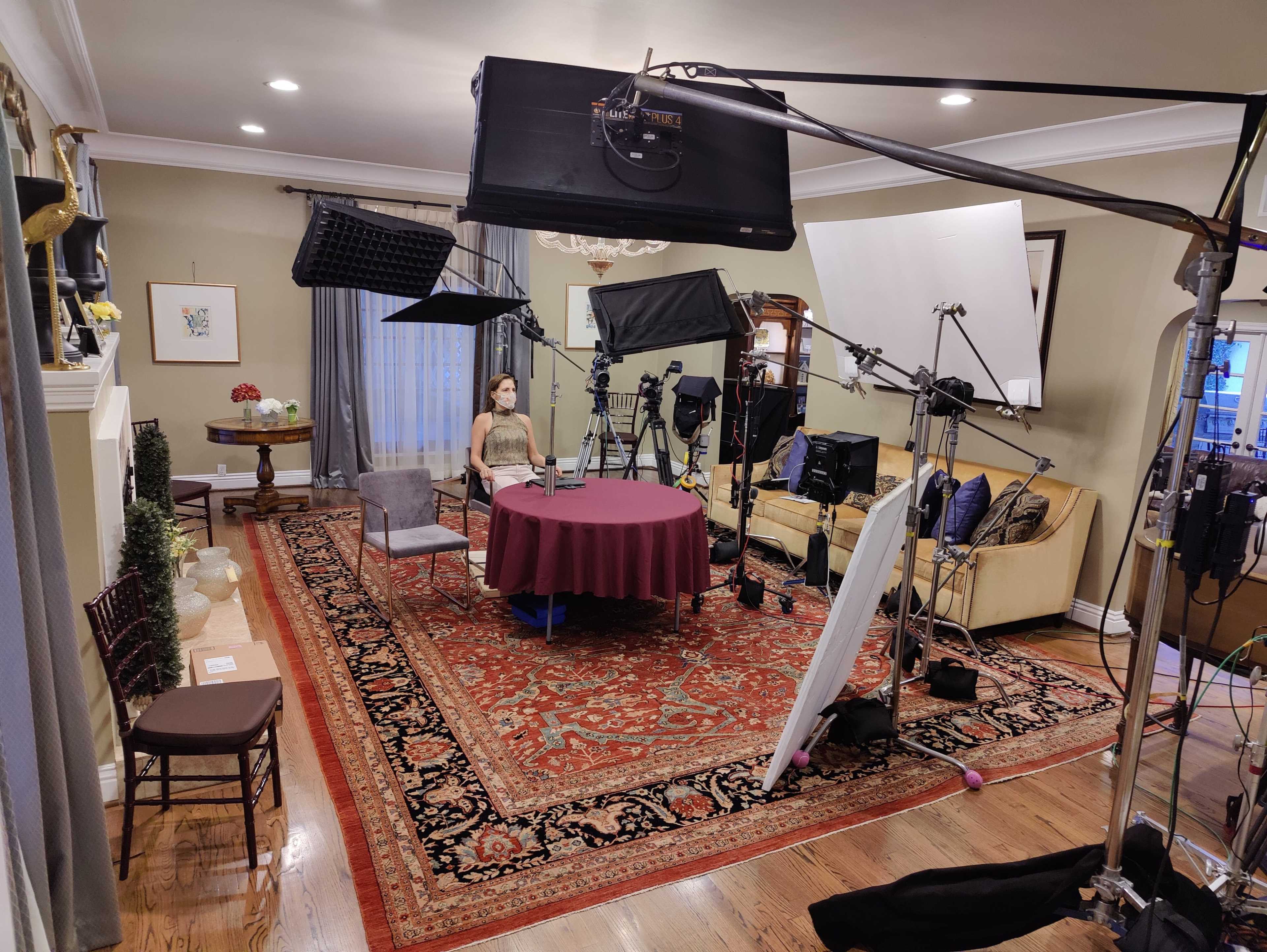 A well-equipped filming set featuring a circular table with a tablecloth, surrounded by various lighting and camera equipment in a living room.