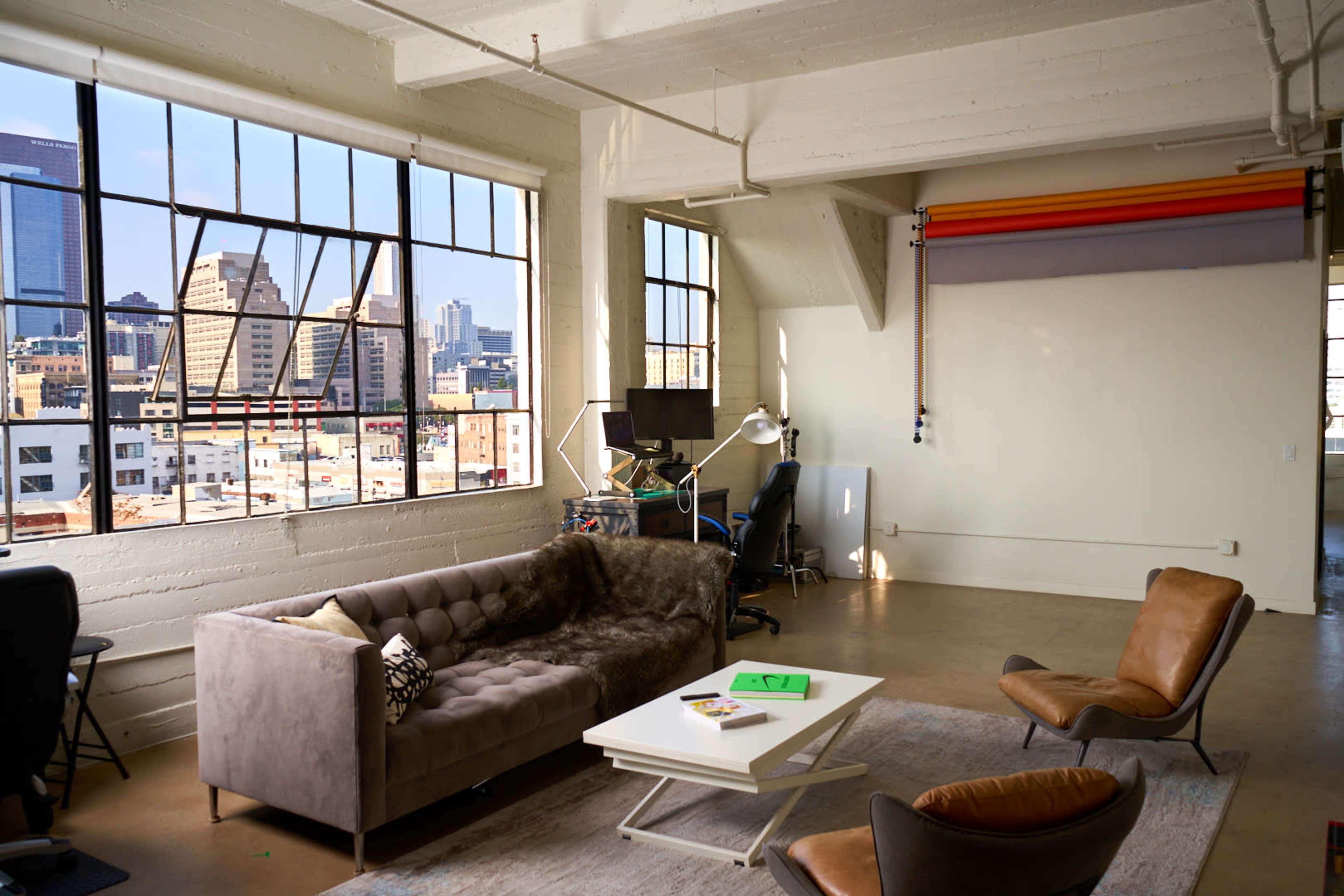 A modern, spacious loft-style living area with large windows, a gray couch, and a coffee table, overlooking a city skyline.