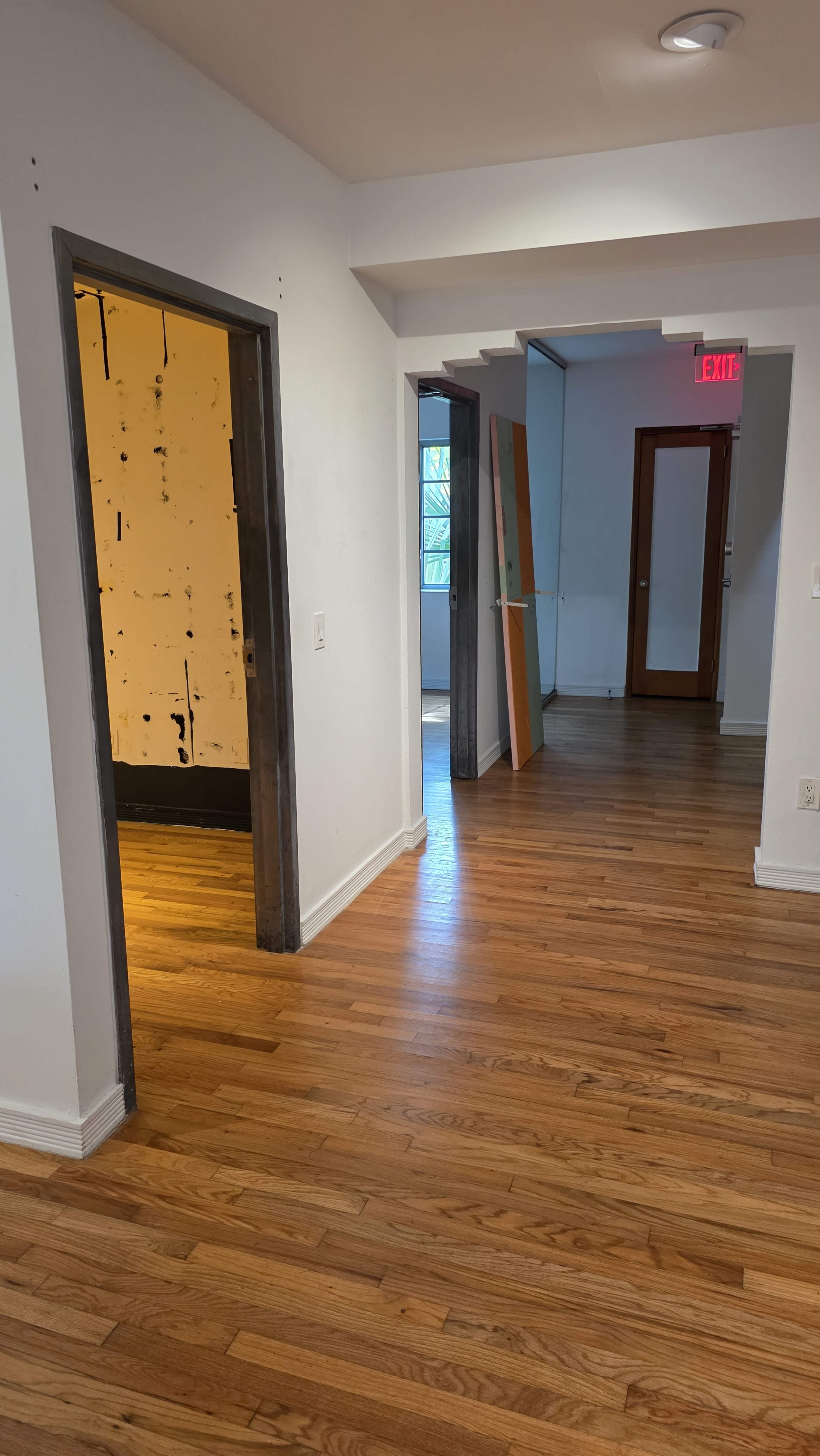 The image shows a hallway with multiple doorways, hardwood floors, and white walls.
