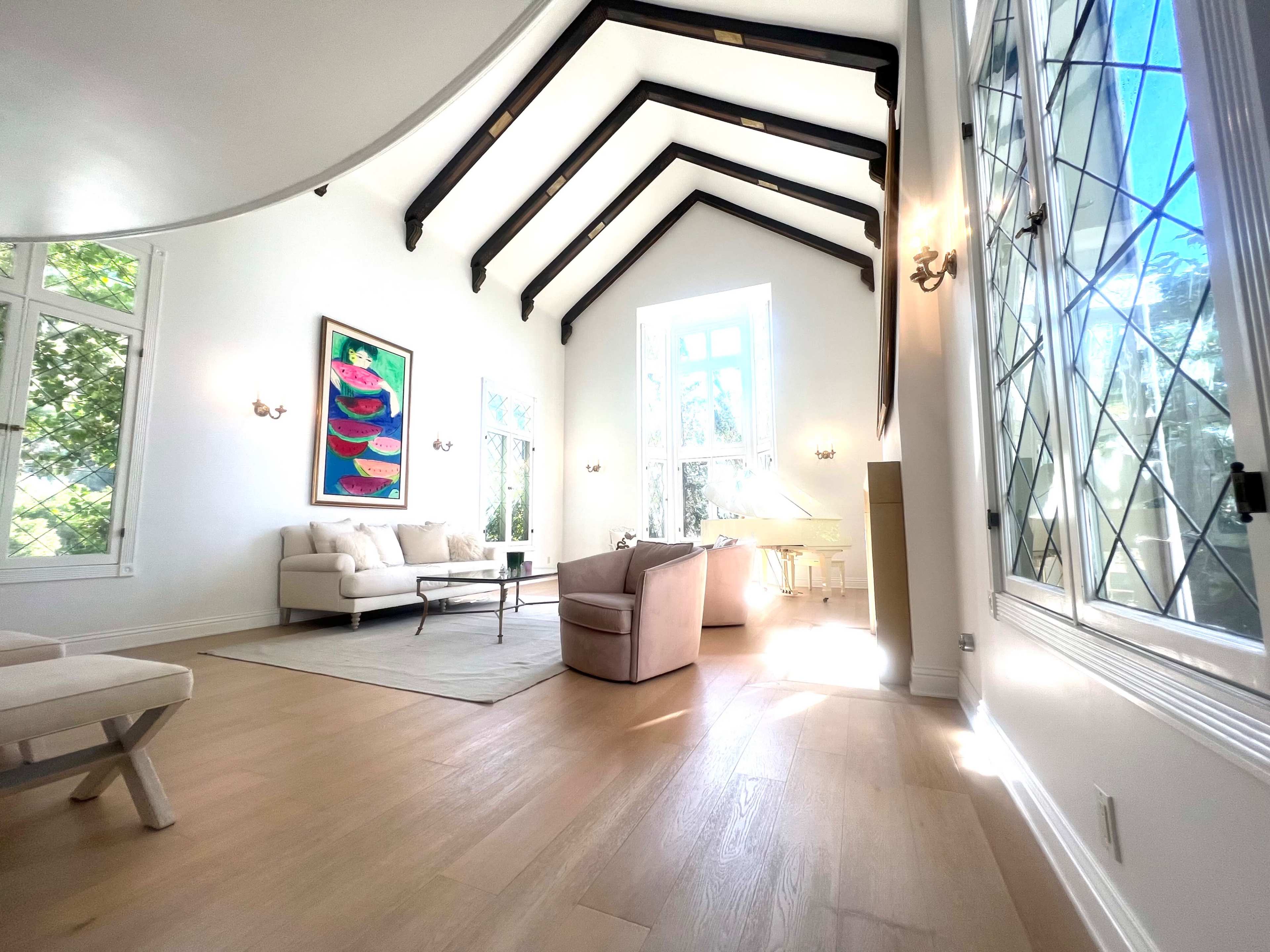 A spacious living room features high, beamed ceilings, large windows, and minimalist furnishings.