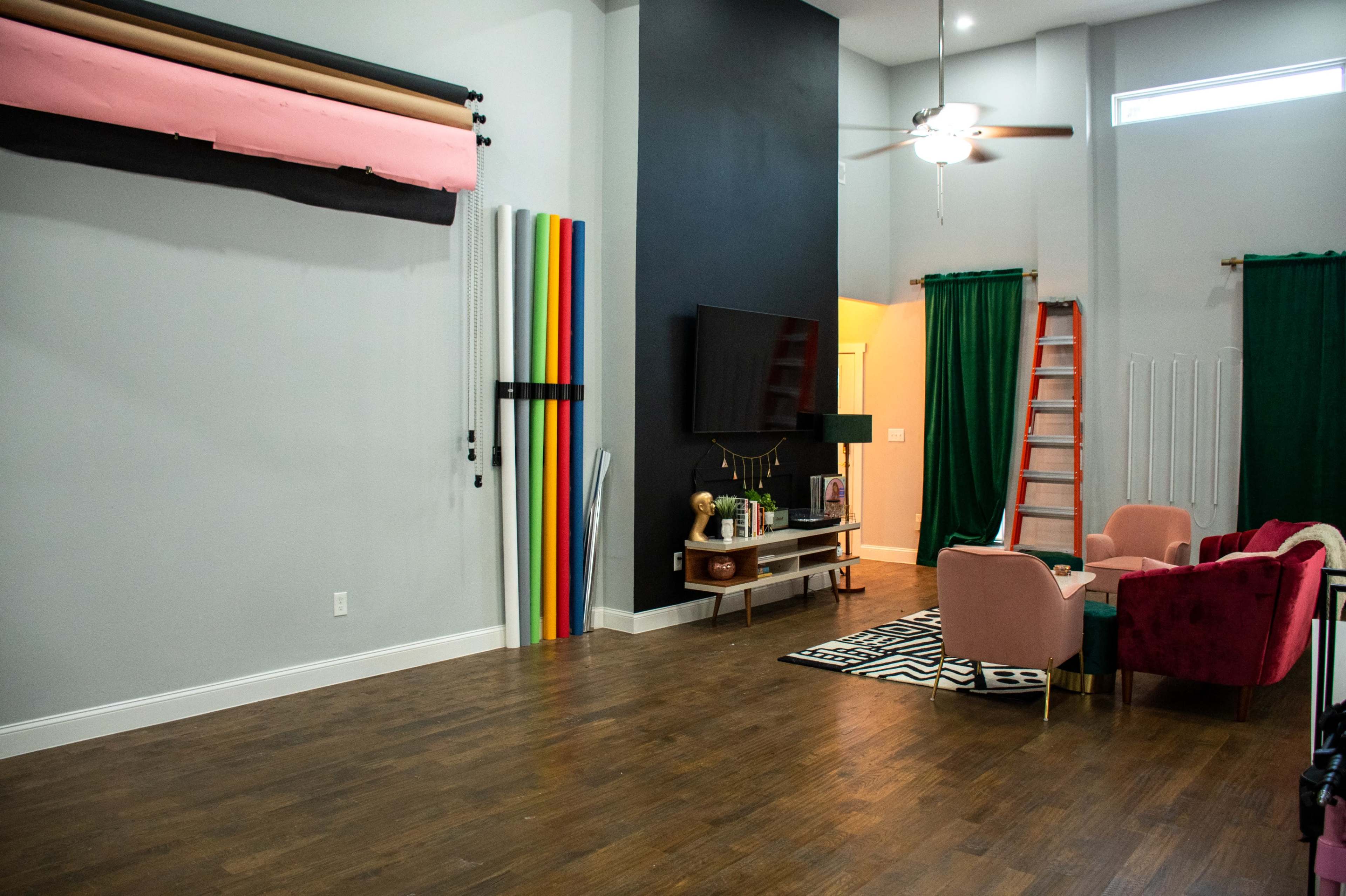 A spacious interior with a wooden floor, colorful backdrops on the wall, a television, two armchairs, and large green drapes.