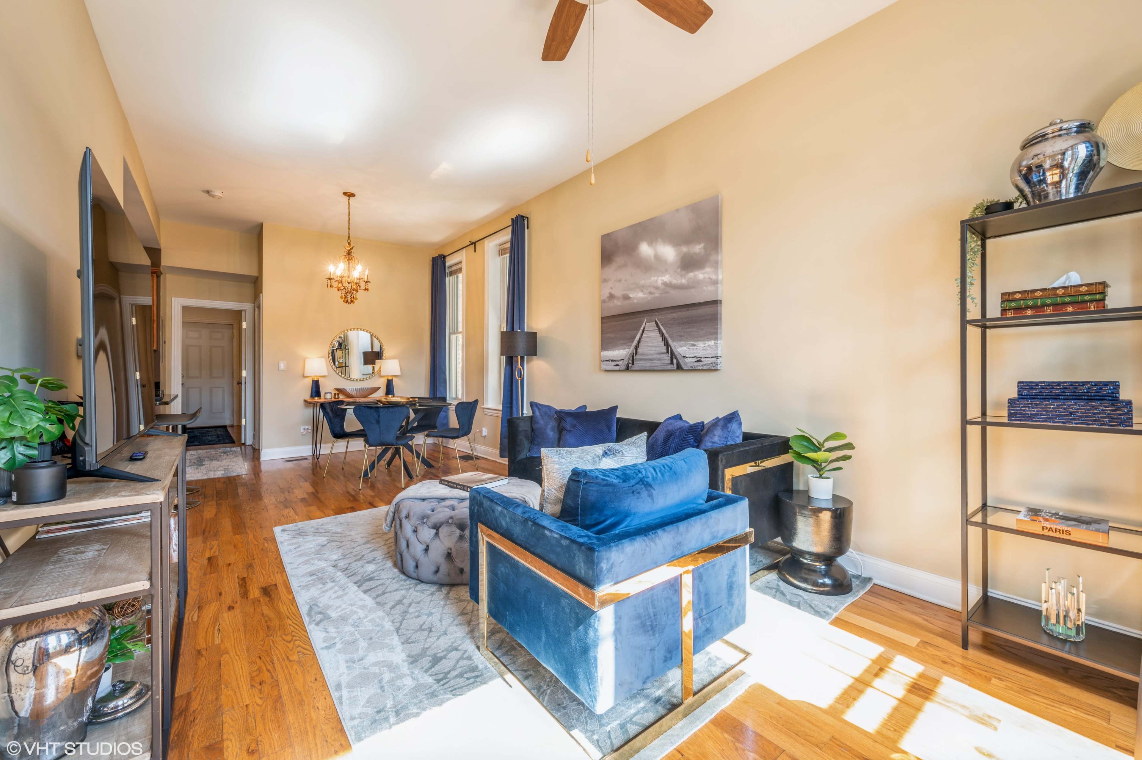 The living room features blue furniture, hardwood floors, and a dining area with a round table and mirror.