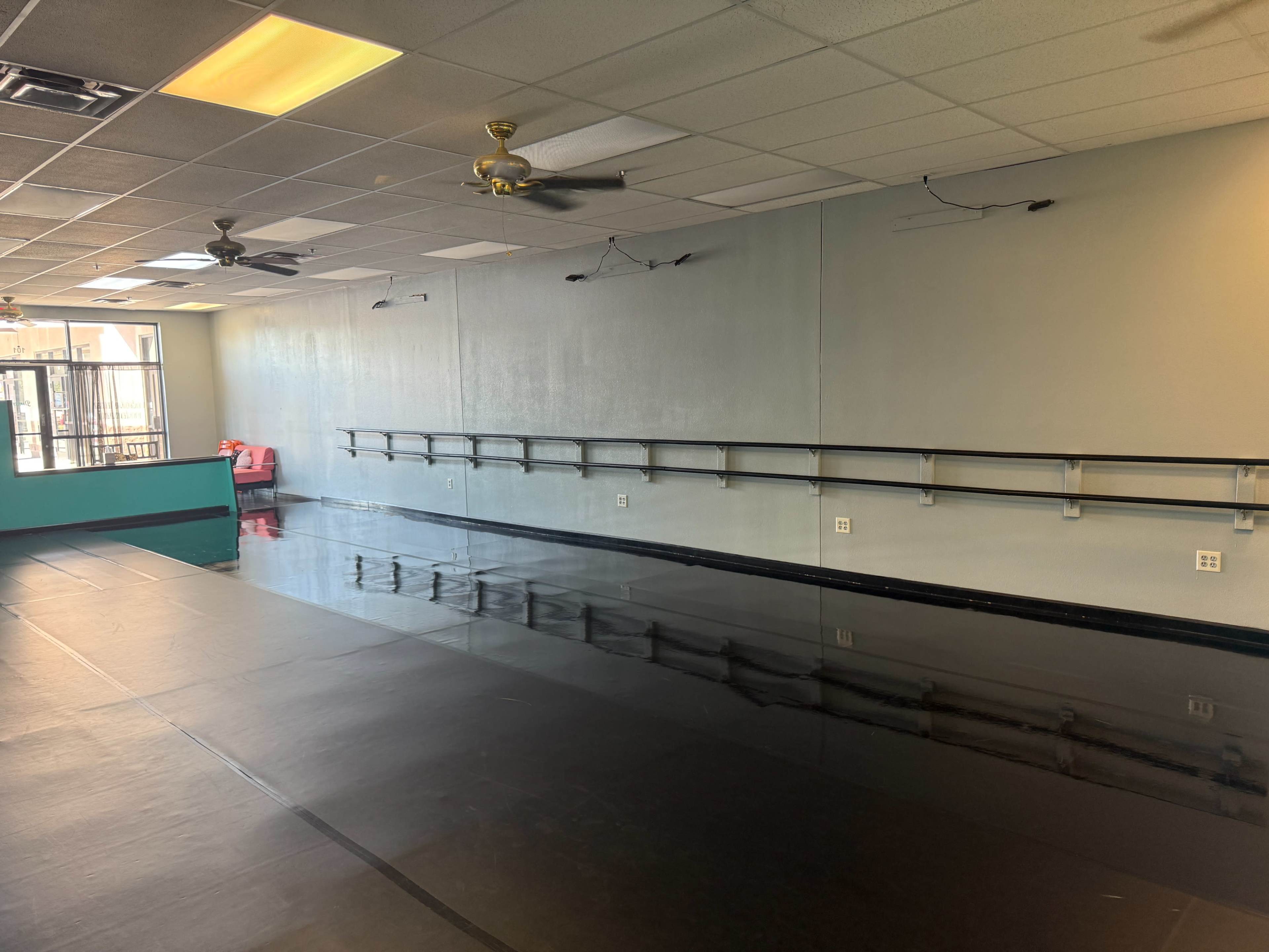 The image shows an empty dance studio with mirrored walls, a black floor, and a row of exercise bars along one side.