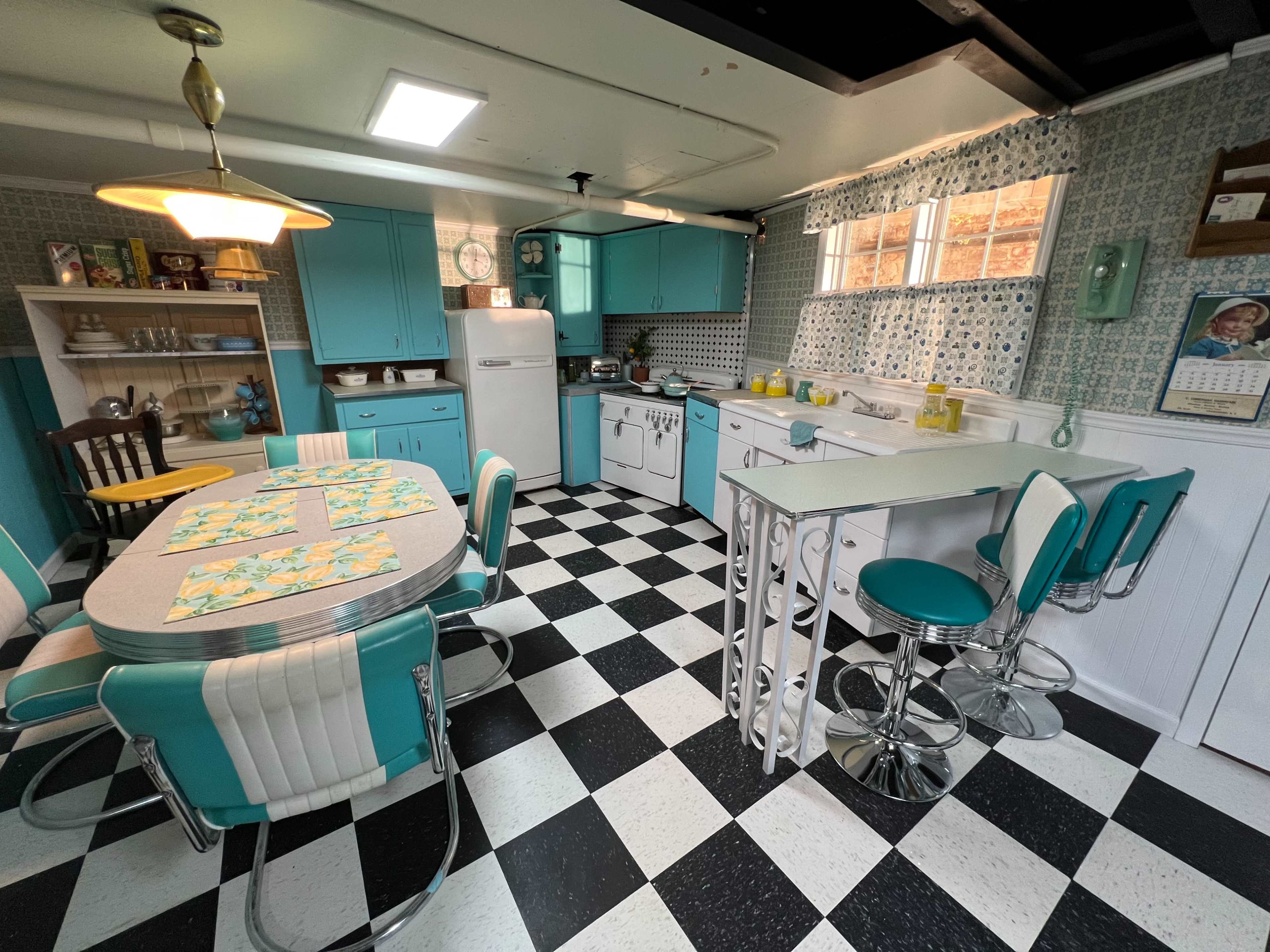 A retro-style kitchen with turquoise cabinets, a checkered black and white floor, and vintage appliances.