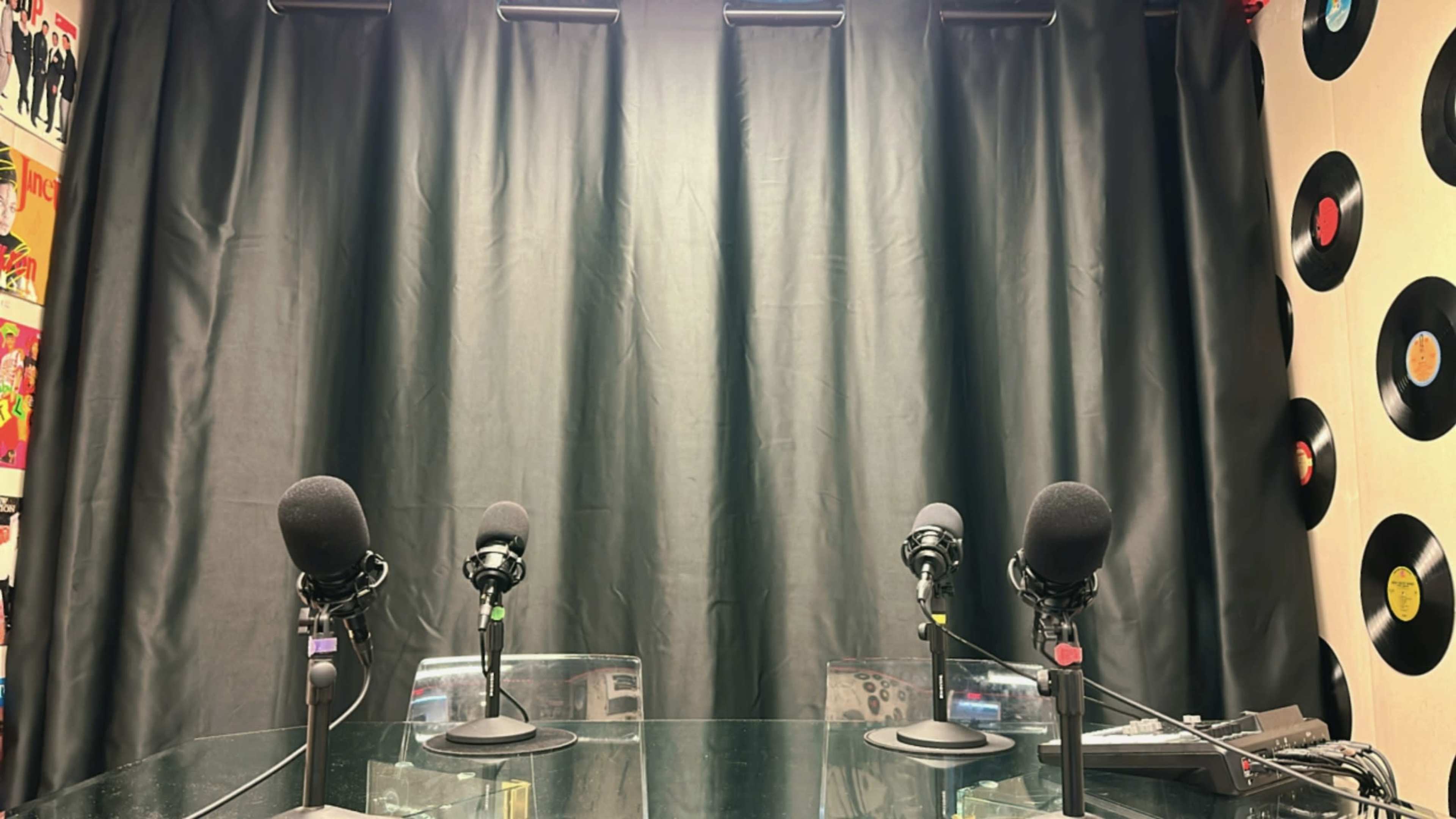 The image shows a recording studio setup with four microphones on stands arranged in front of a black curtain, illuminated from above.