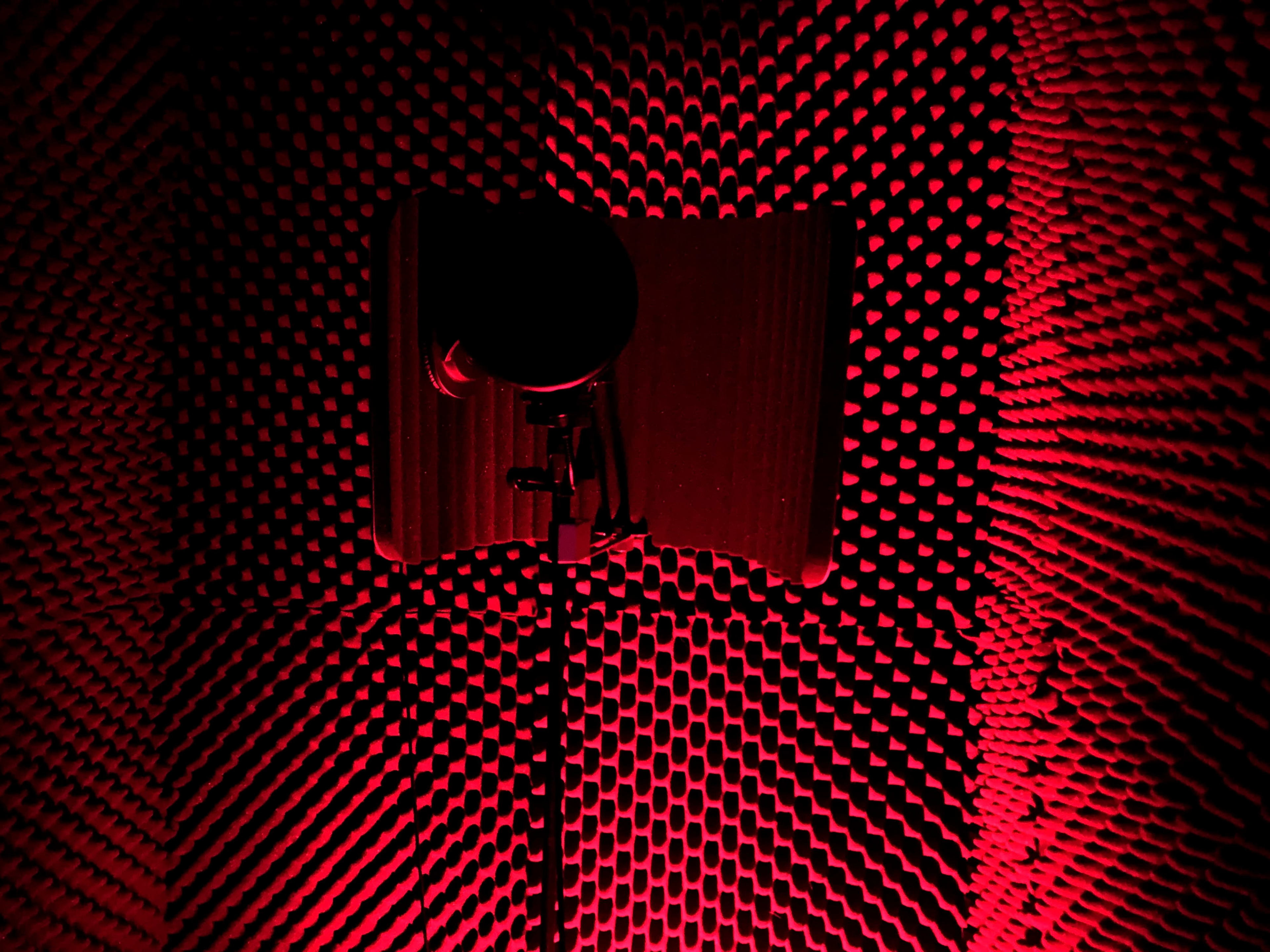 A microphone set up in a soundproof recording booth with red lighting.