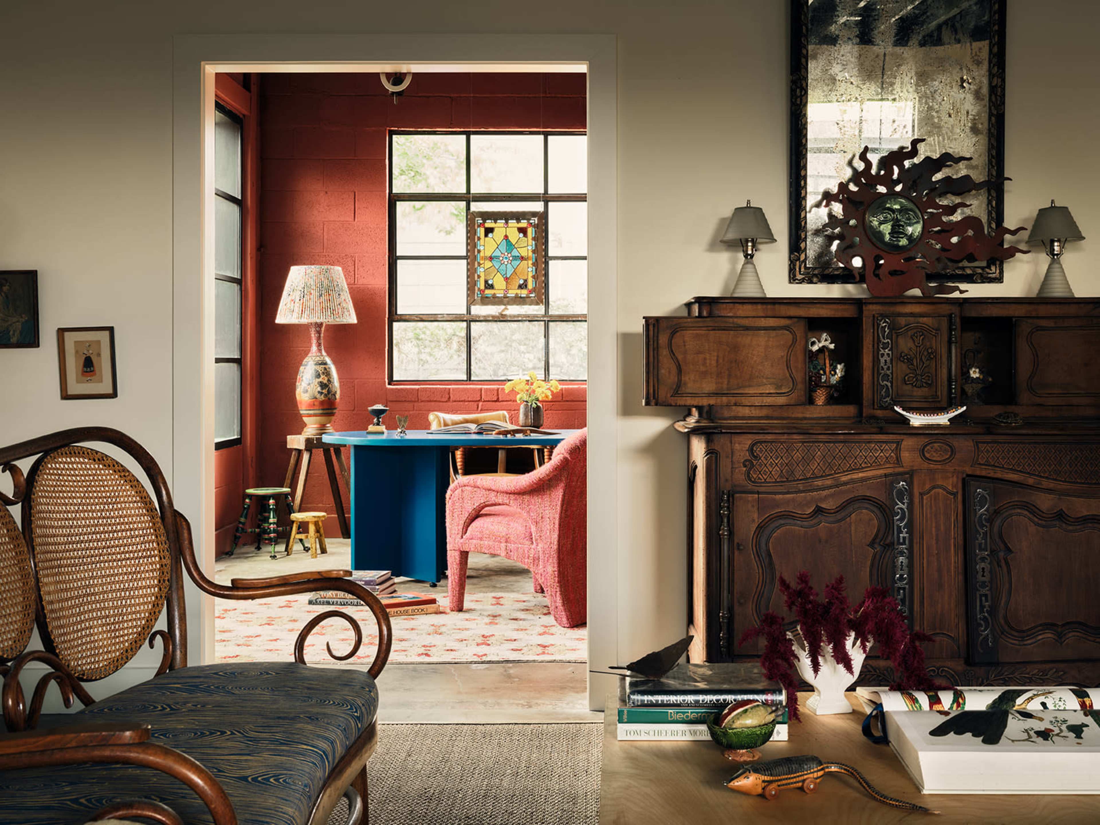 The image shows a stylish interior space featuring a wooden sideboard, various artworks, and a living area with red walls and modern furniture.