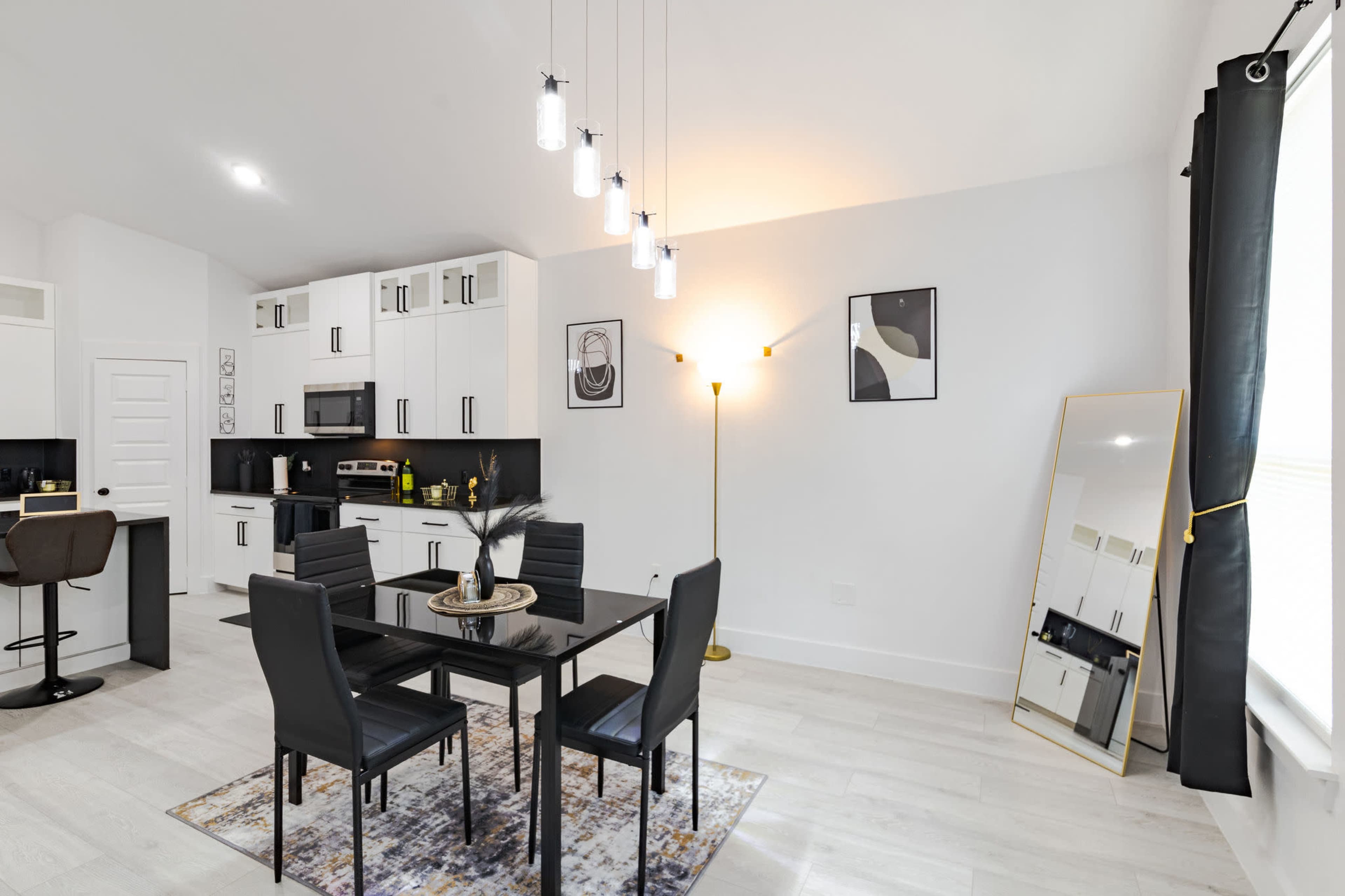 The image shows a modern kitchen and dining area featuring a black and white color scheme, a dining table with four chairs, and pendant lighting above.