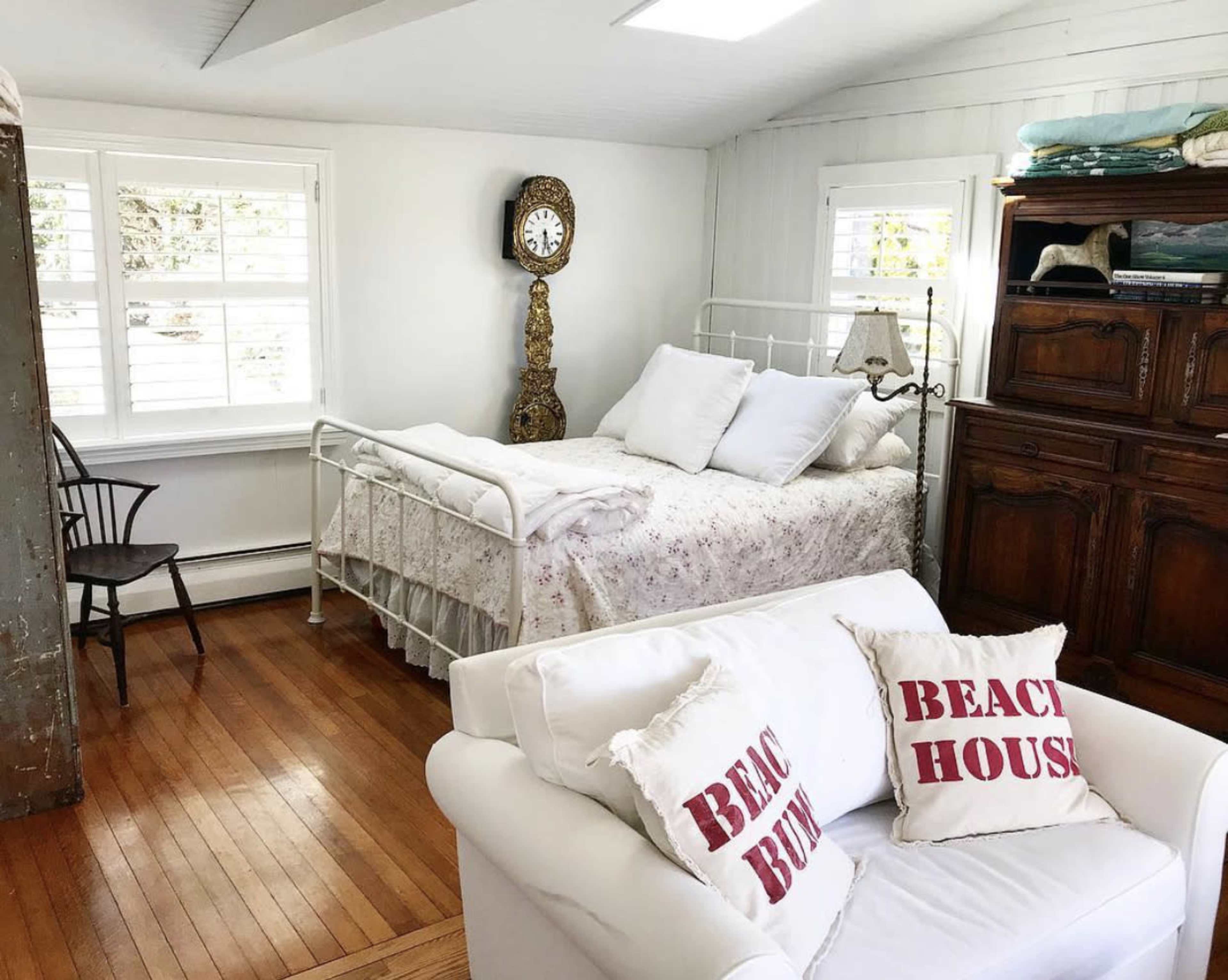 The room features a white bed with floral bedding, two decorative pillows stating "BEACH BUM," and a wooden dresser against the wall.