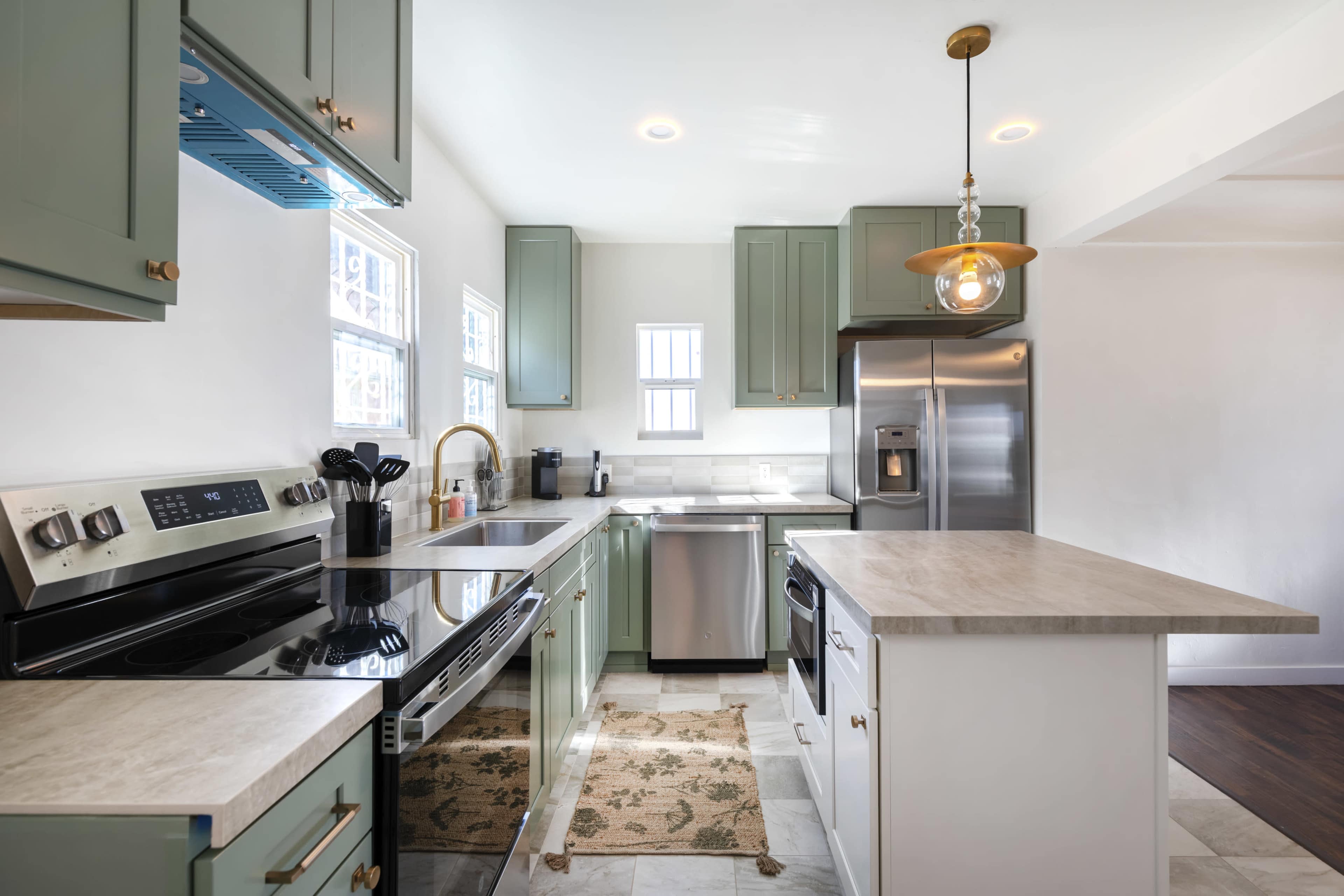 The kitchen features green cabinetry, stainless steel appliances, and a central island with a quartz countertop.