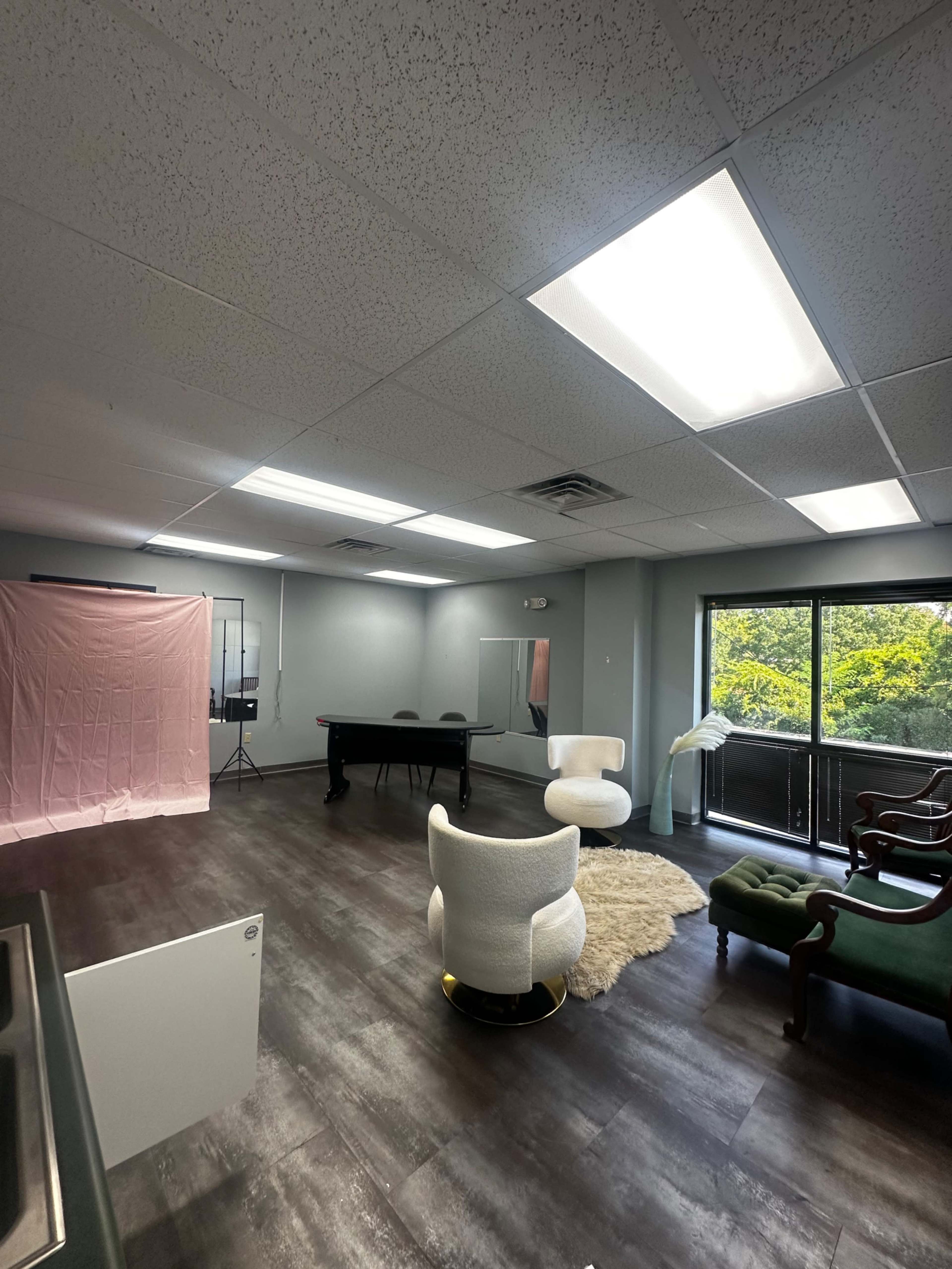 The image shows a spacious interior room with a pool table, a white lounge chair, a green vintage chair, and a pink backdrop set up for photography.