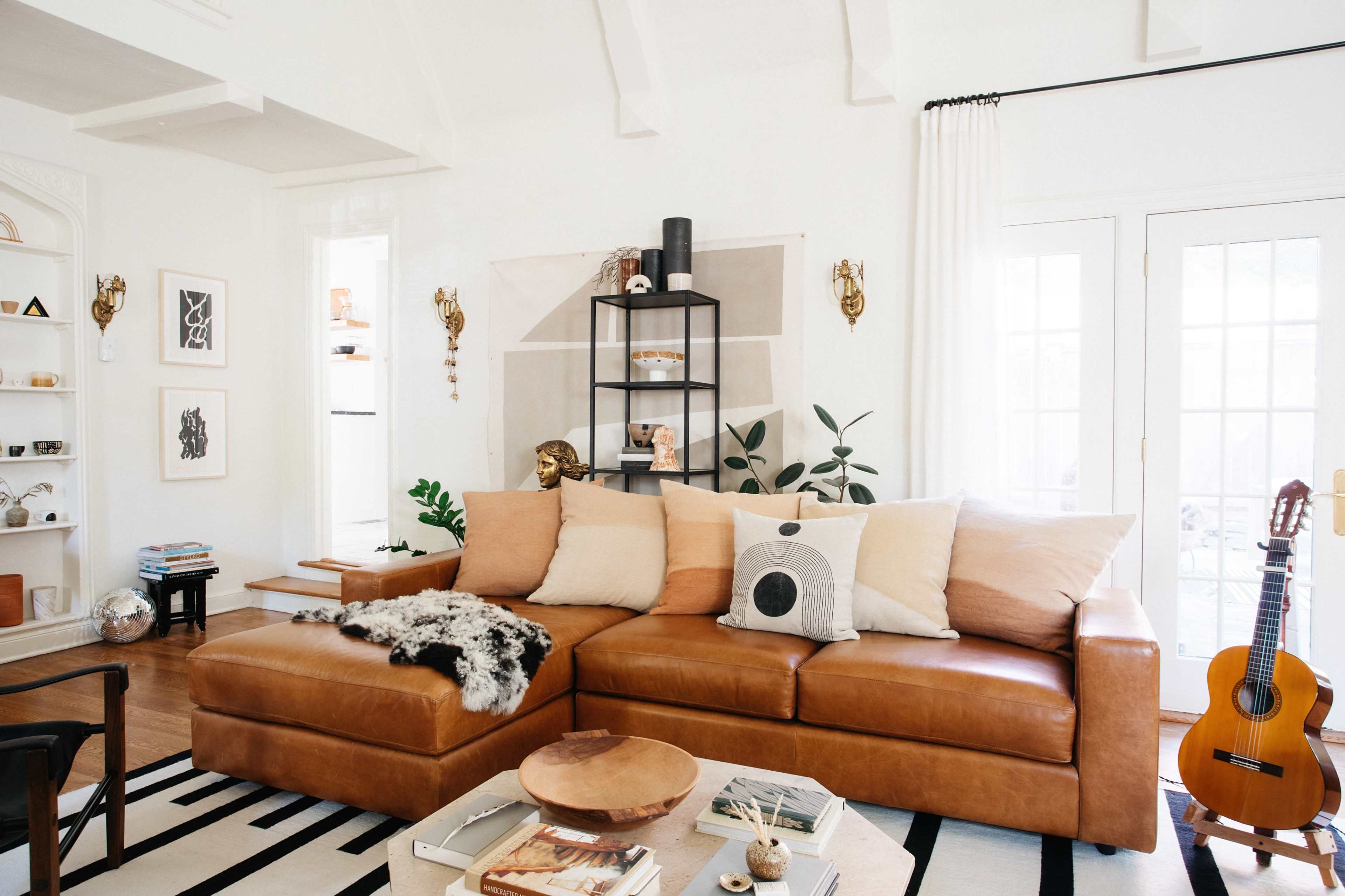 A modern living room features a large brown leather sectional sofa, a wooden coffee table, decorative plants, and a guitar displayed in a corner.