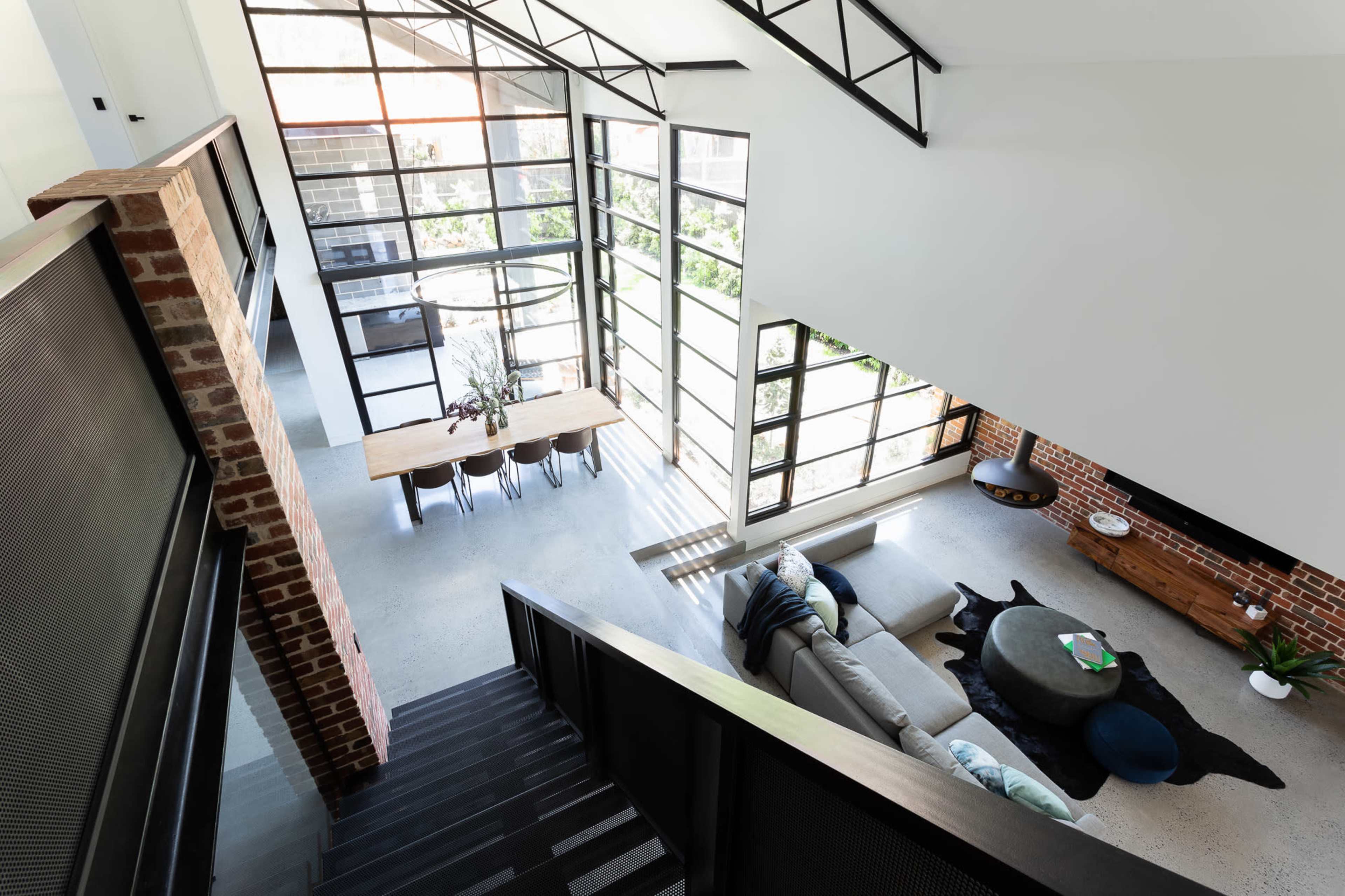A spacious, modern living area with large windows, a dining table, and a staircase leading to a lower level.
