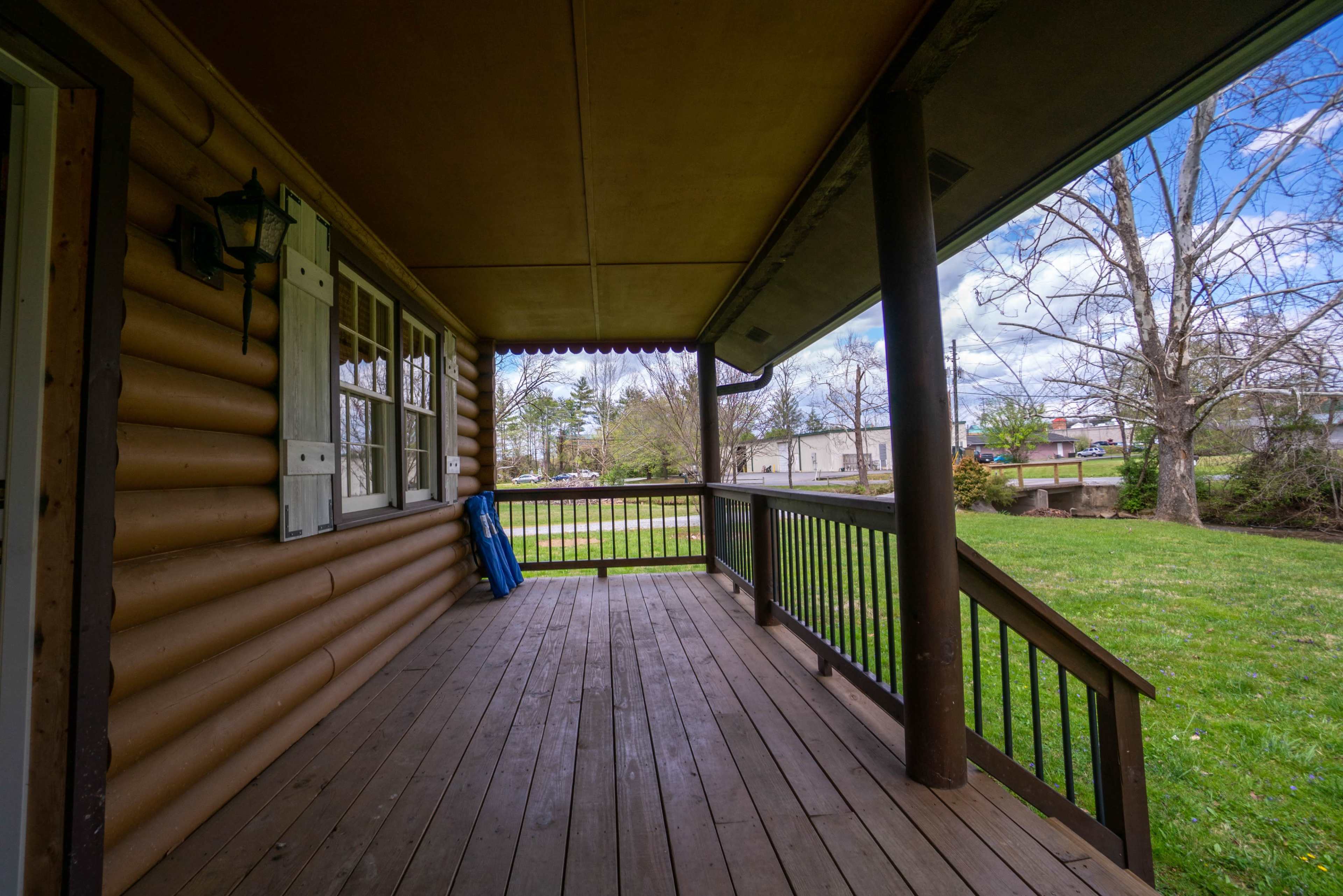 The image shows a wooden porch with a view of an expansive grassy area and trees beyond.