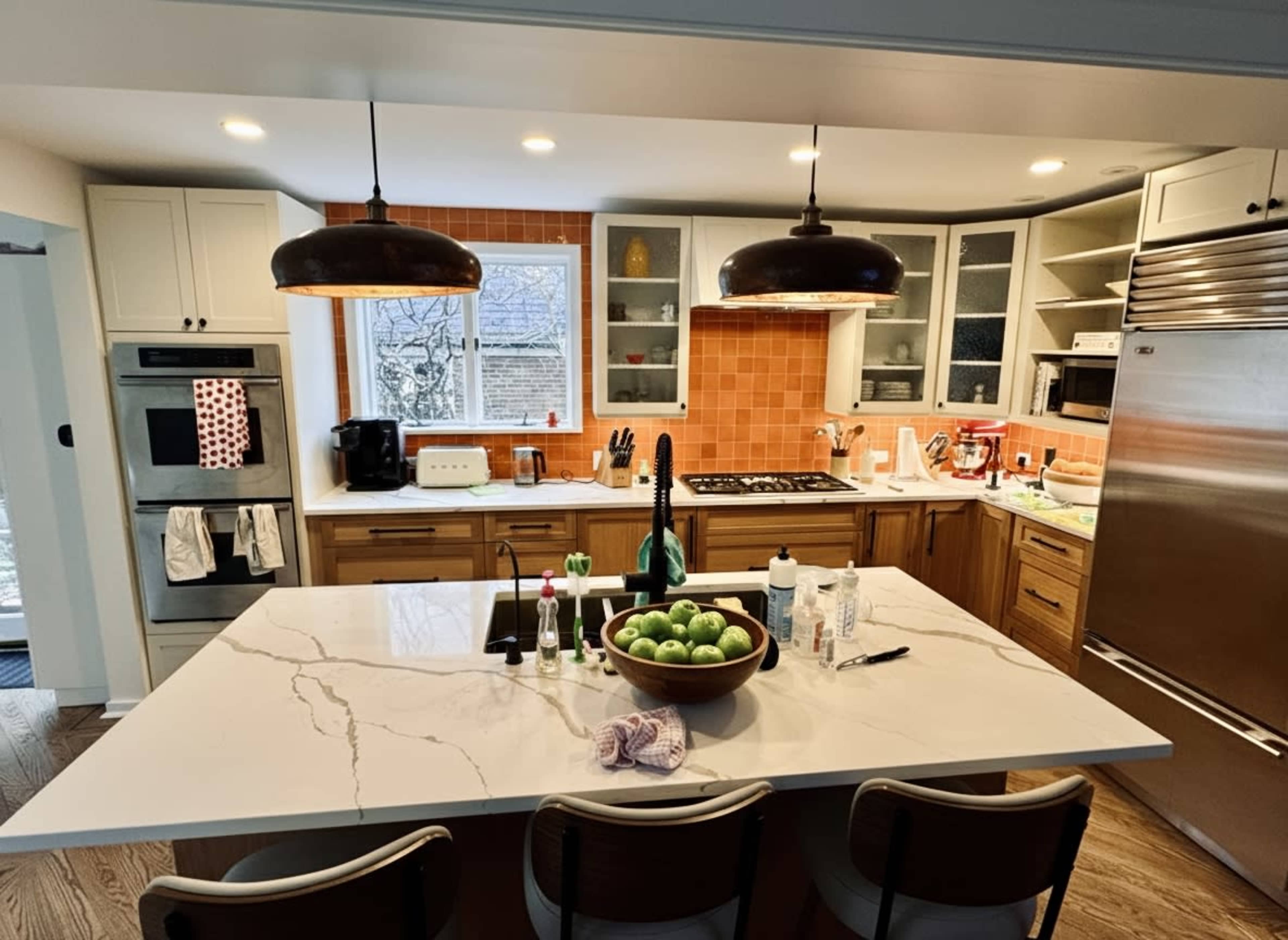 The kitchen features wooden cabinets, a large island with a marble countertop, and a backsplash of orange tiles.