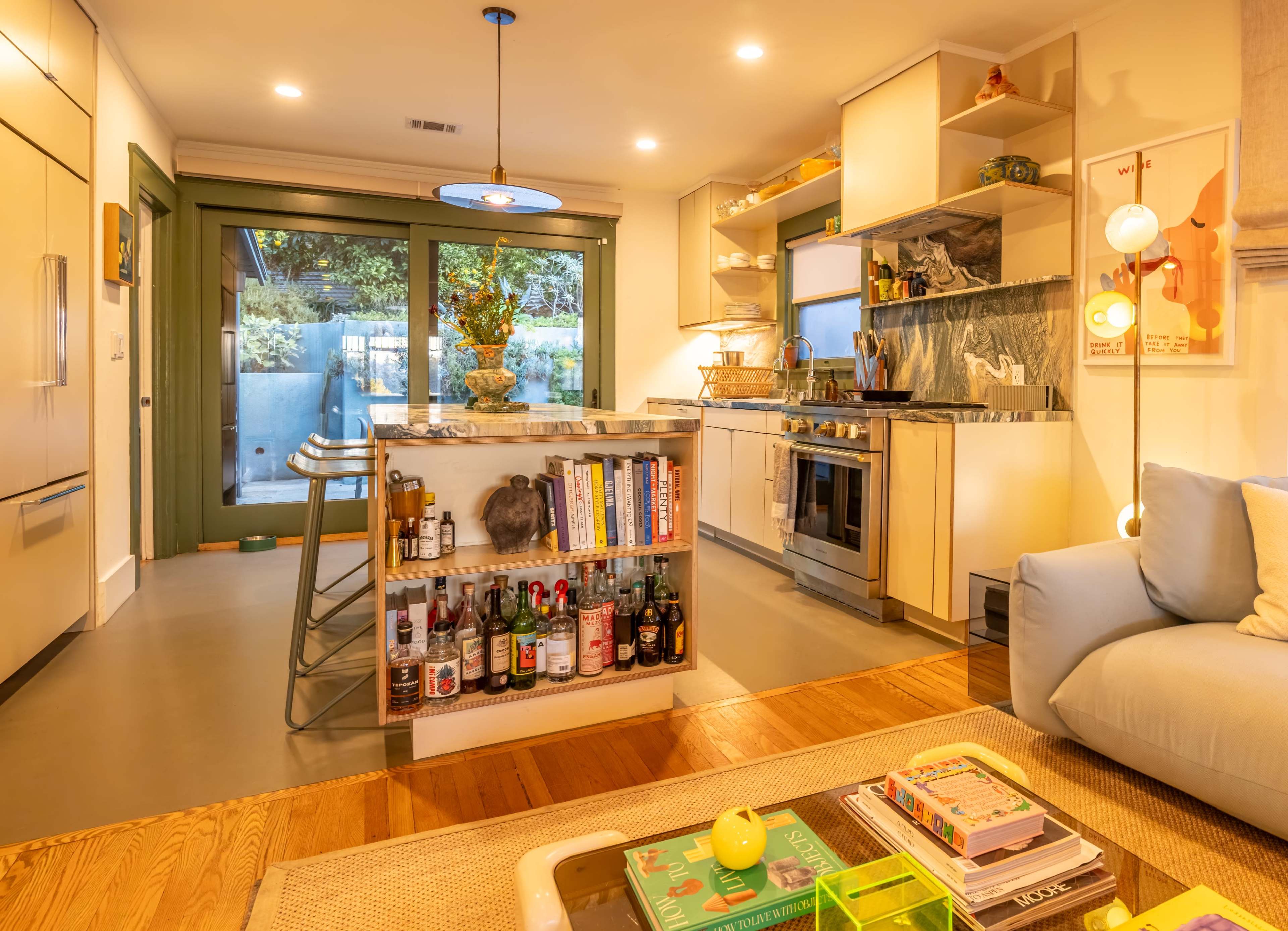 The image shows a modern kitchen with a bar area and an open layout, featuring a mix of cabinetry, marble countertops, and large glass doors leading to an outdoor space.