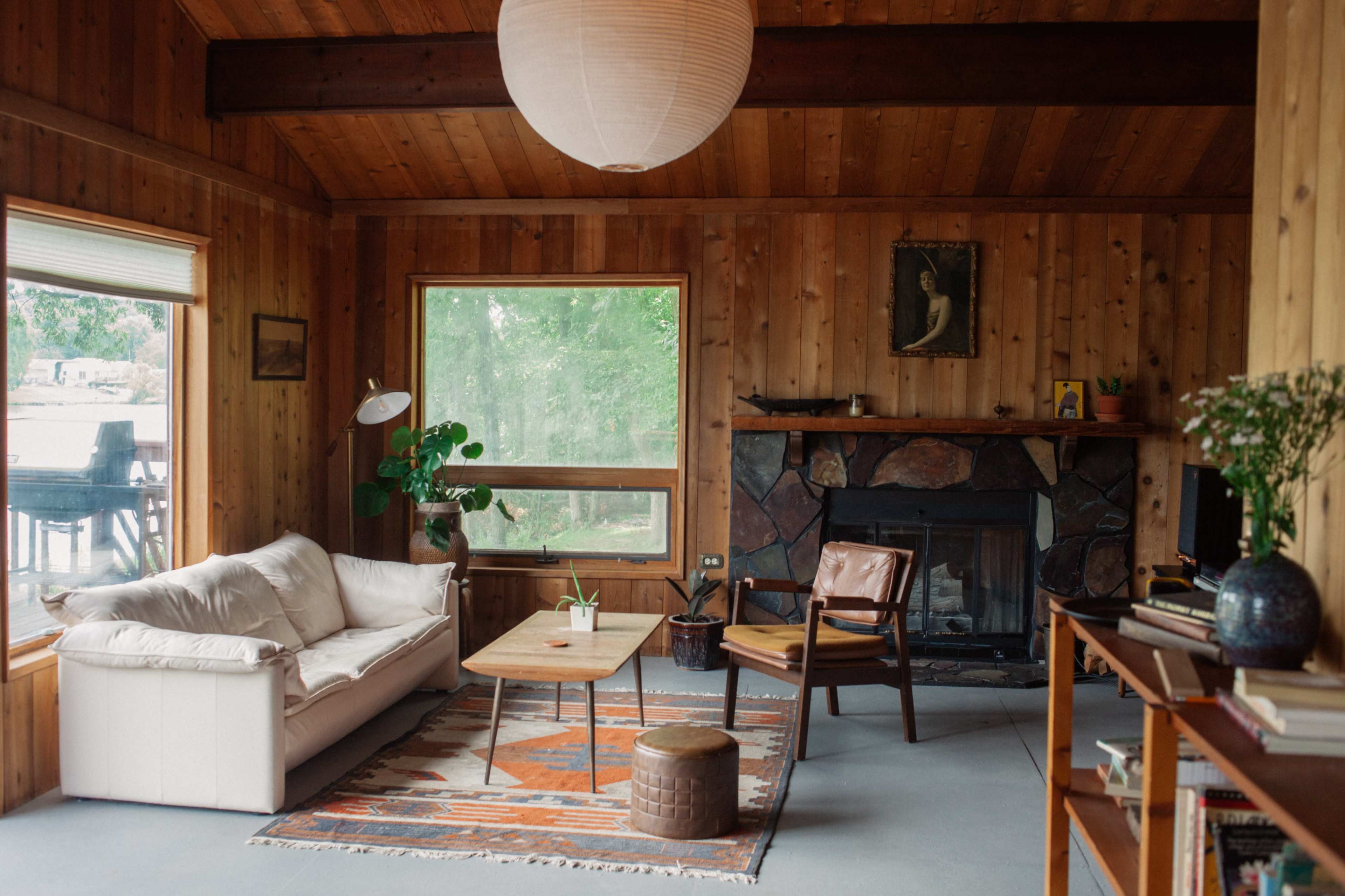 A wooden-paneled living room with a white sofa, a wooden coffee table, and a large window overlooking greenery.