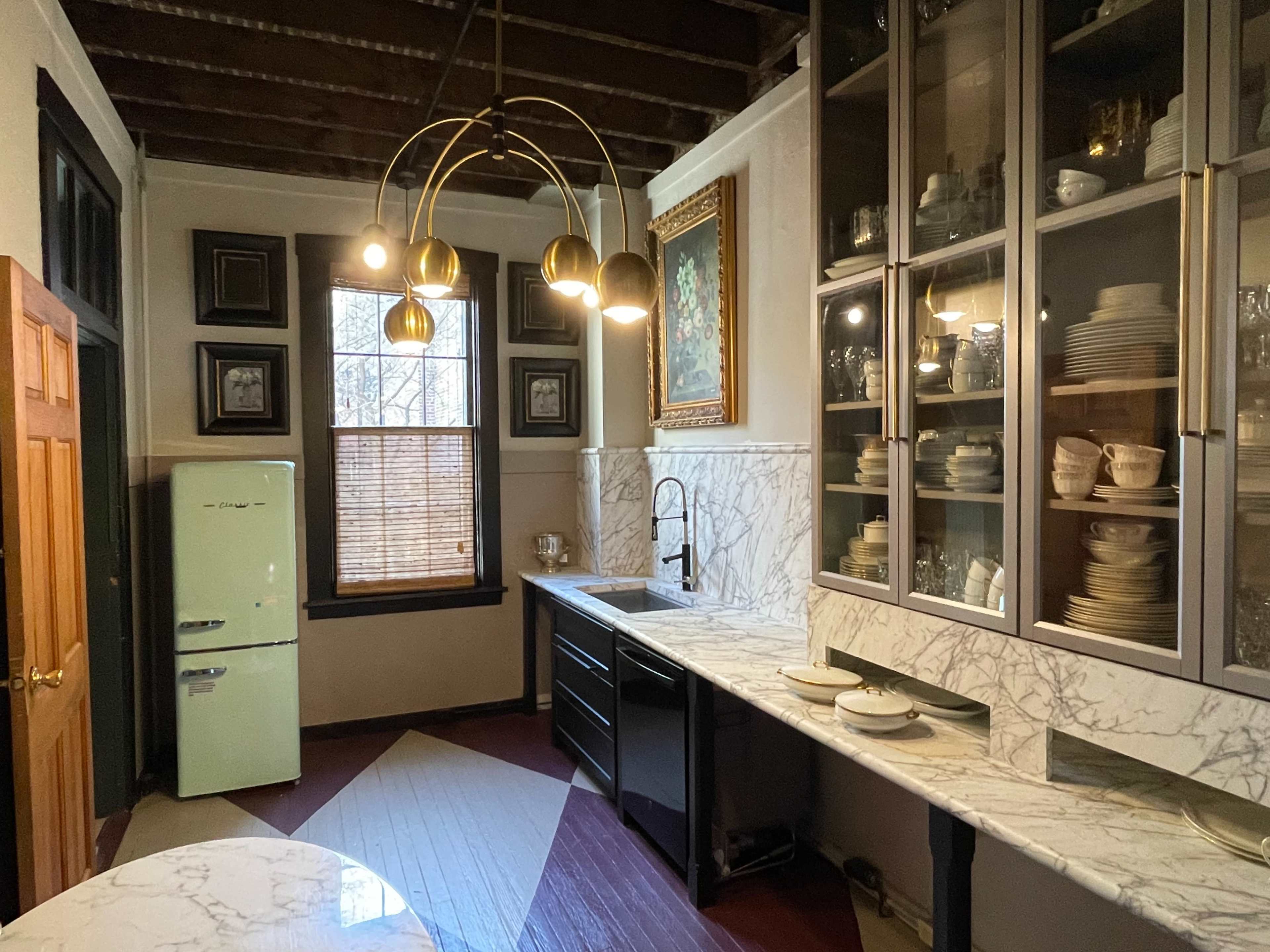 The kitchen features a marble countertop, a black cabinet, a vintage green refrigerator, and a set of glass-fronted cabinets displaying various dishes.