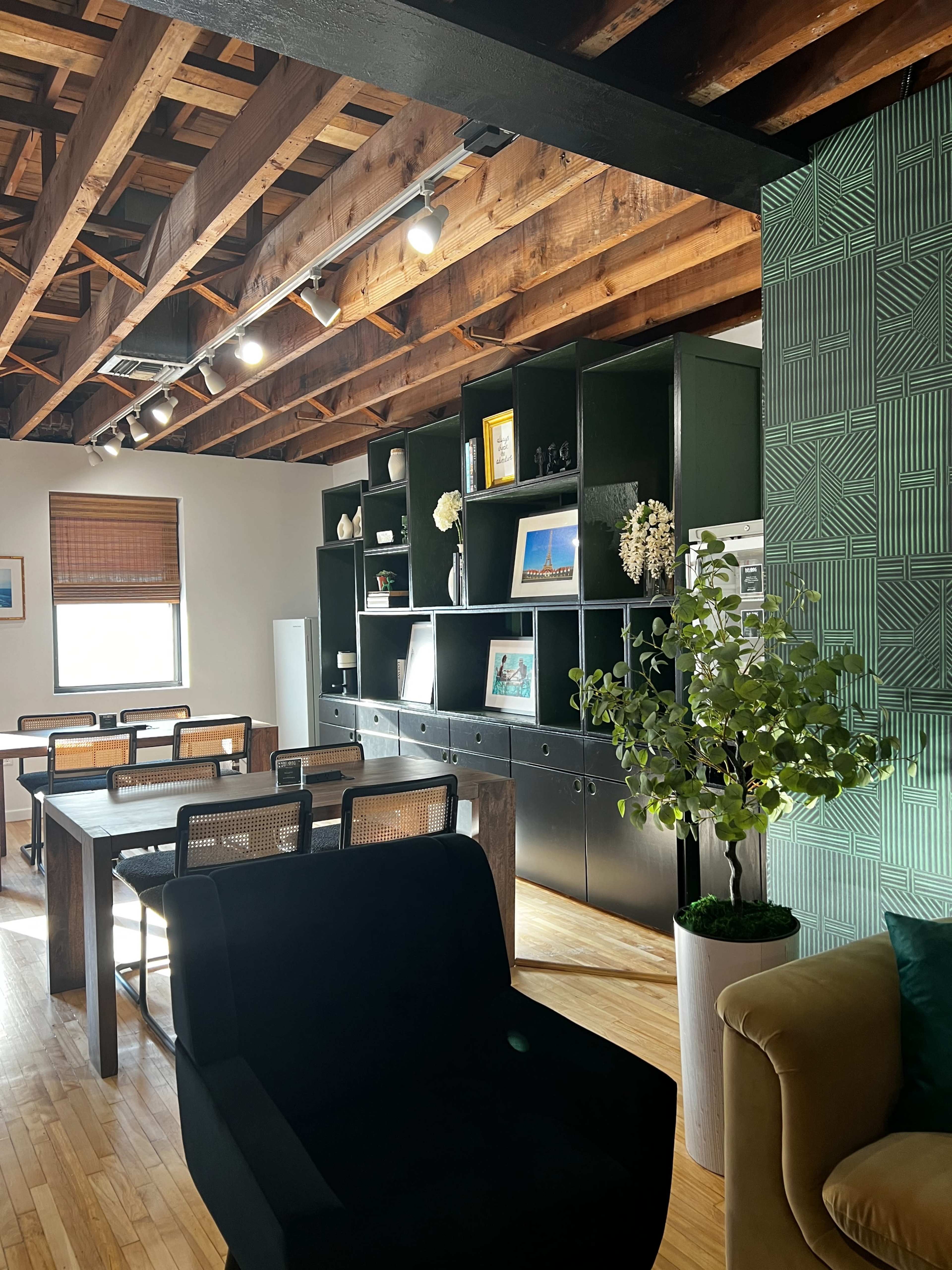 The image shows a modern interior space featuring a black shelving unit, wooden furniture, and a green wall with textured panels.
