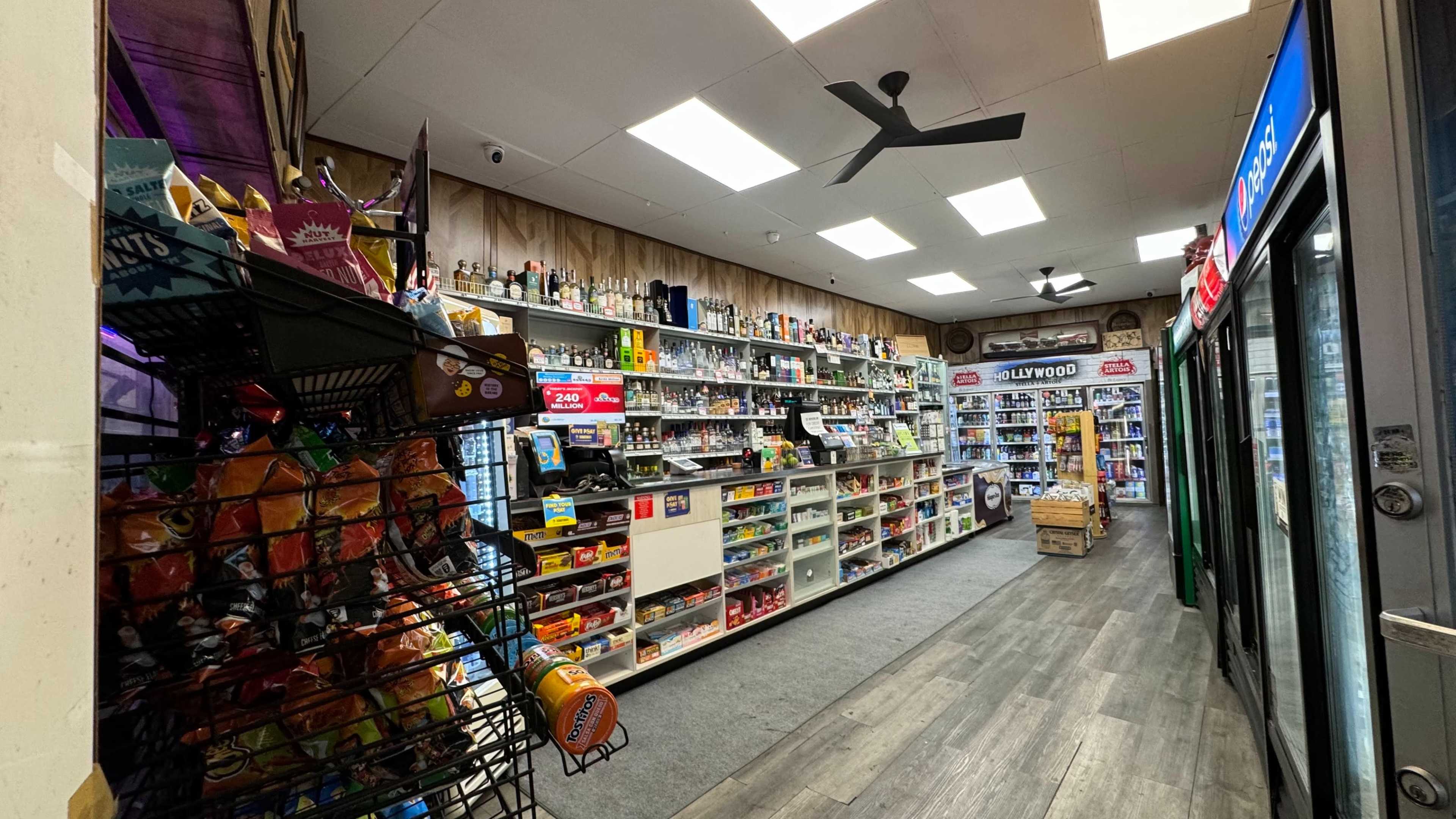 The image shows the interior of a convenience store with shelves stocked with various grocery items and beverages, and a display of snacks in the foreground.