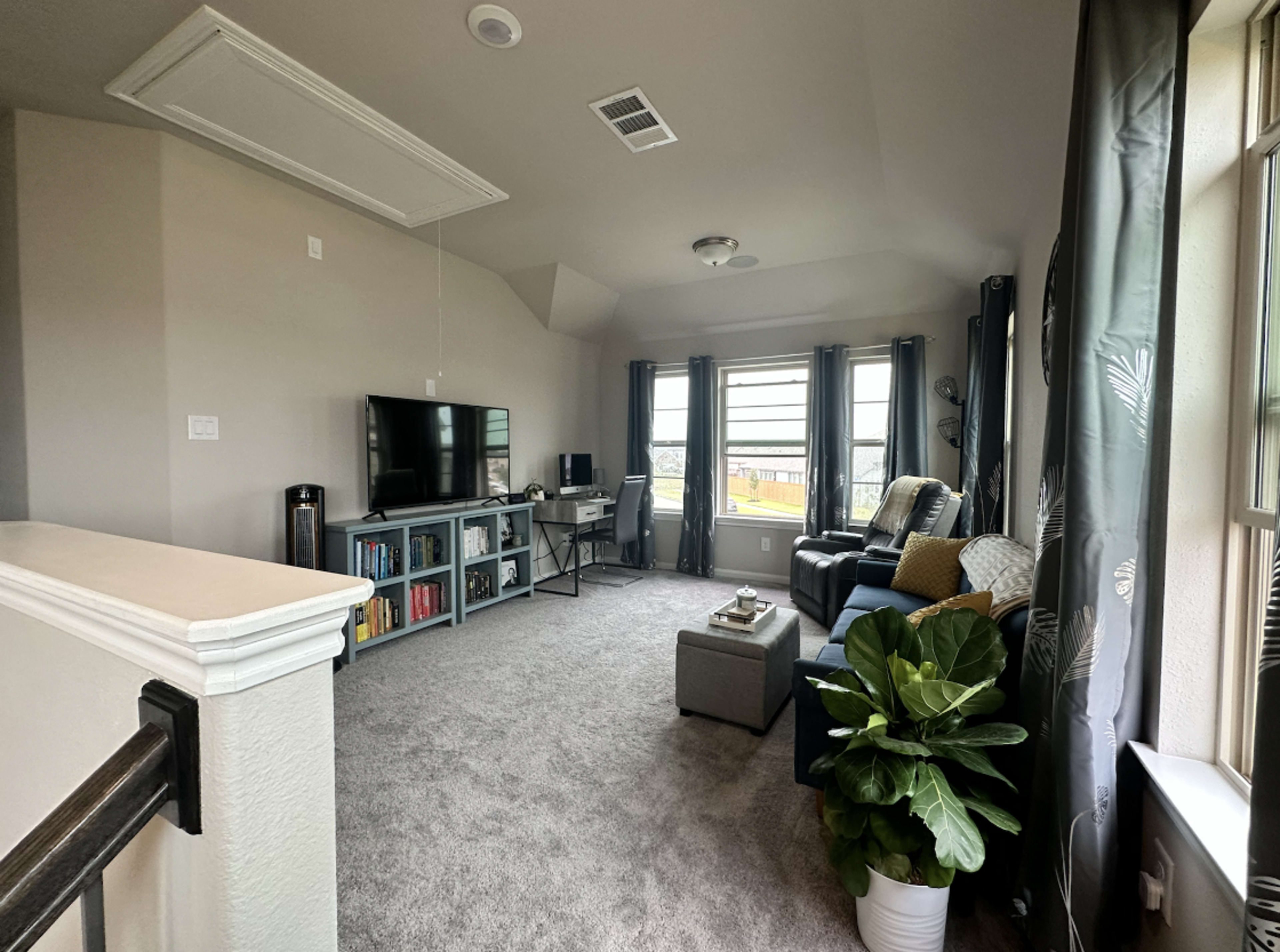 A well-furnished living room with a television on a wall-mounted stand, a cozy couch, a coffee table, and large windows letting in natural light.