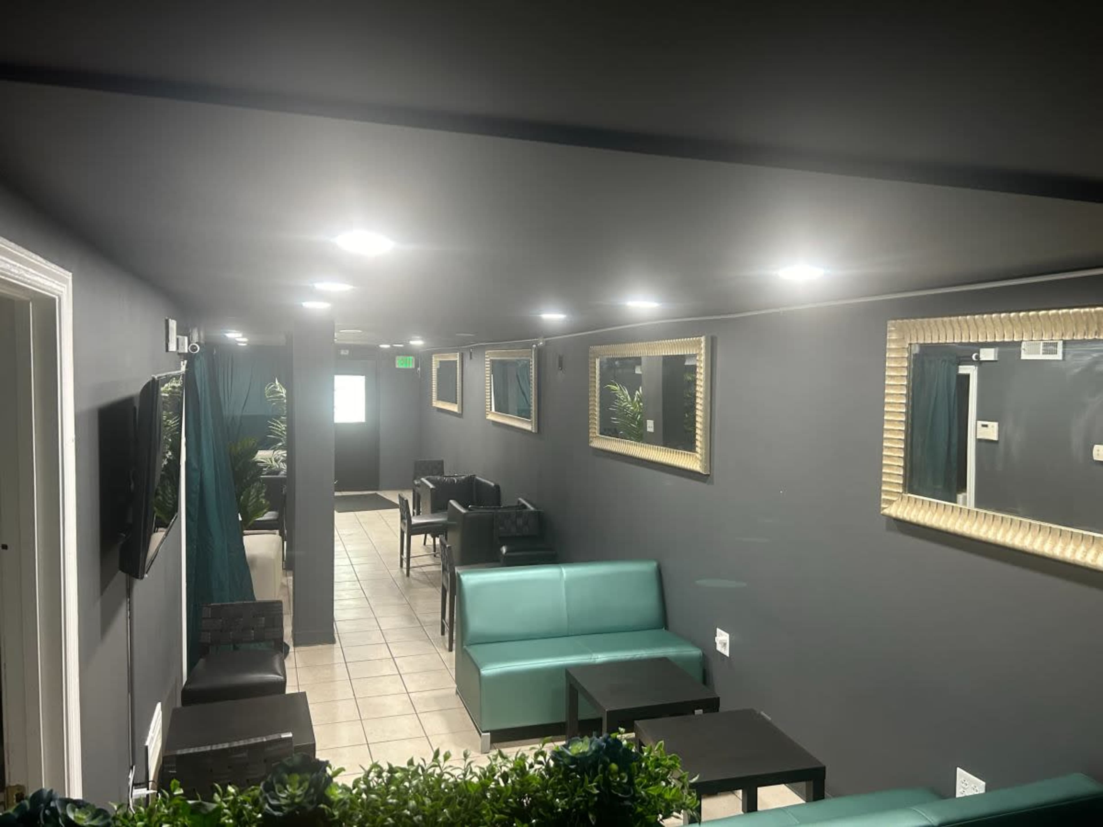 A dimly lit lounge area with teal seating, black tables, and mirrors on the gray walls.