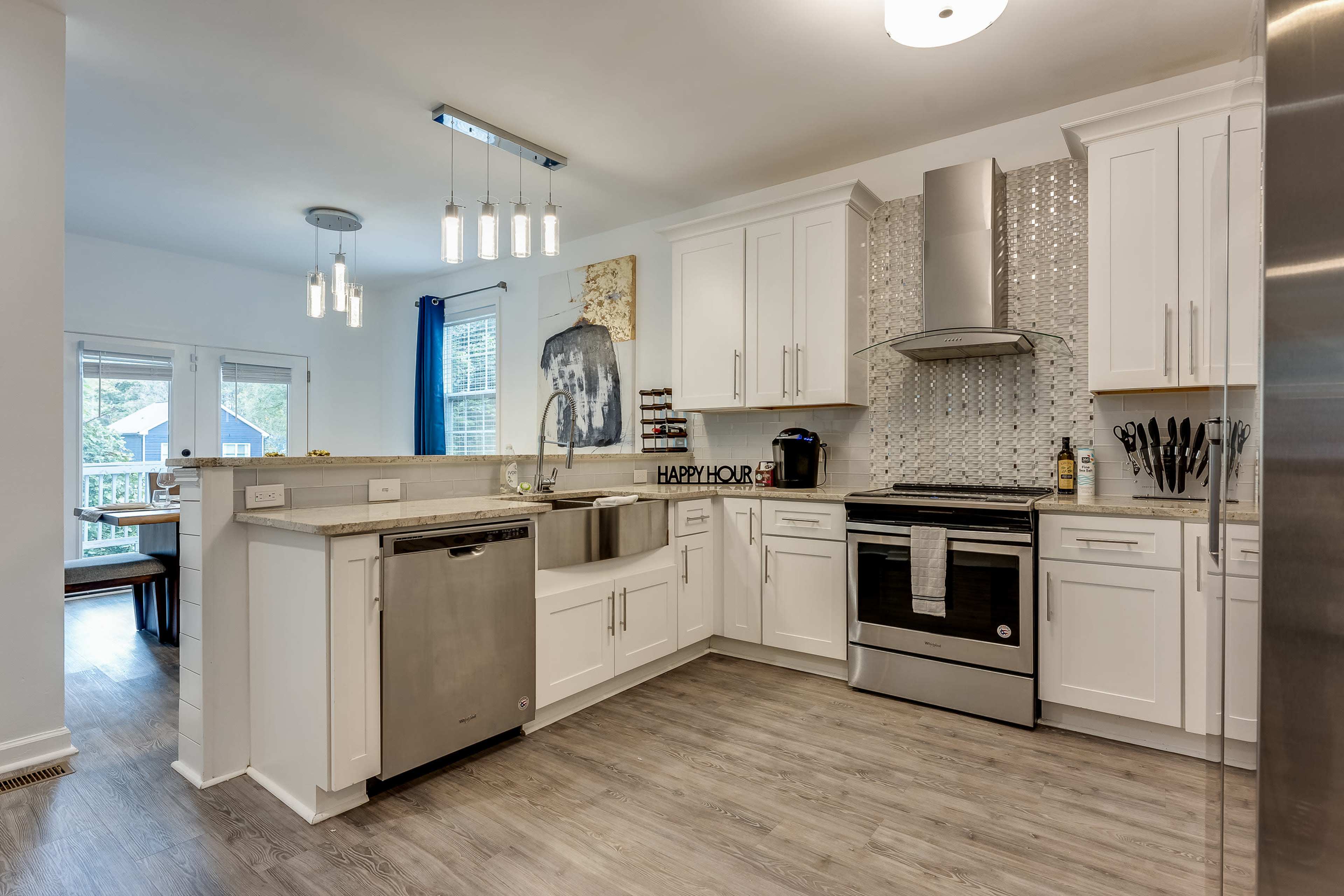The kitchen features white cabinets, a stainless steel appliances, and a large sink, with a dining area visible in the background.