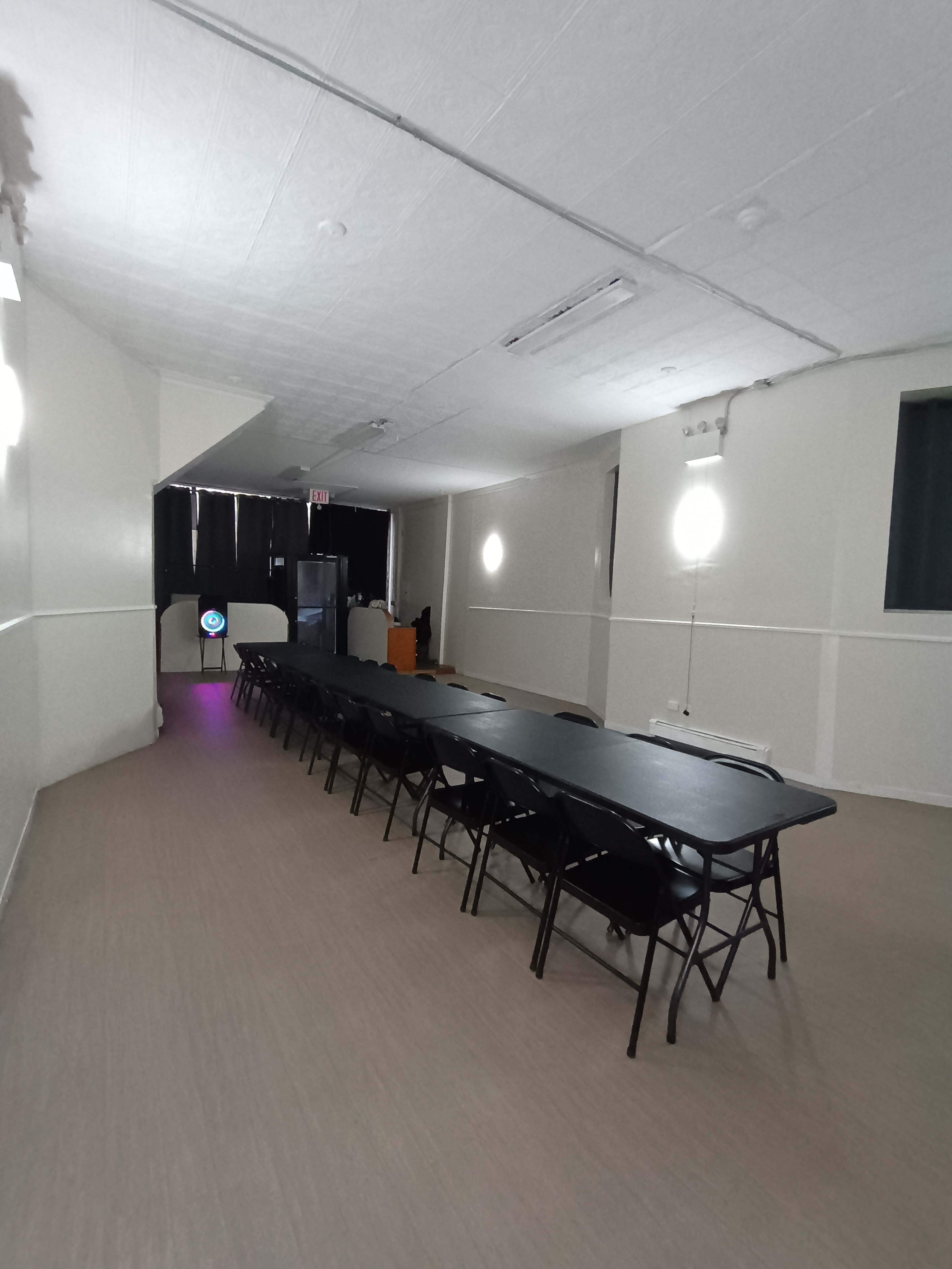 A long rectangular table with chairs is arranged in a spacious, empty room with beige walls and a soft gray floor.