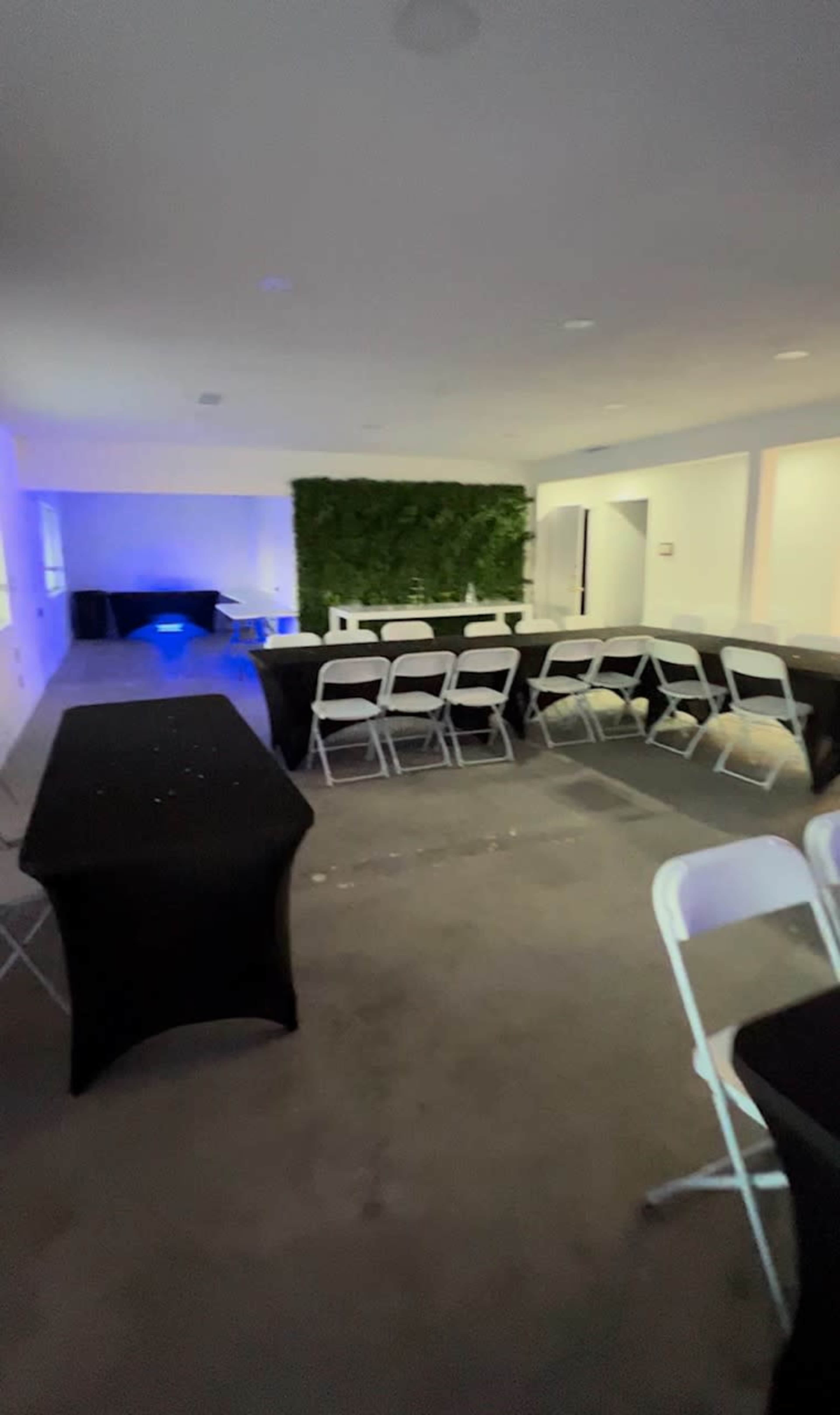 The image shows an empty event space with black and white chairs arranged around several tables, and a green wall in the background.