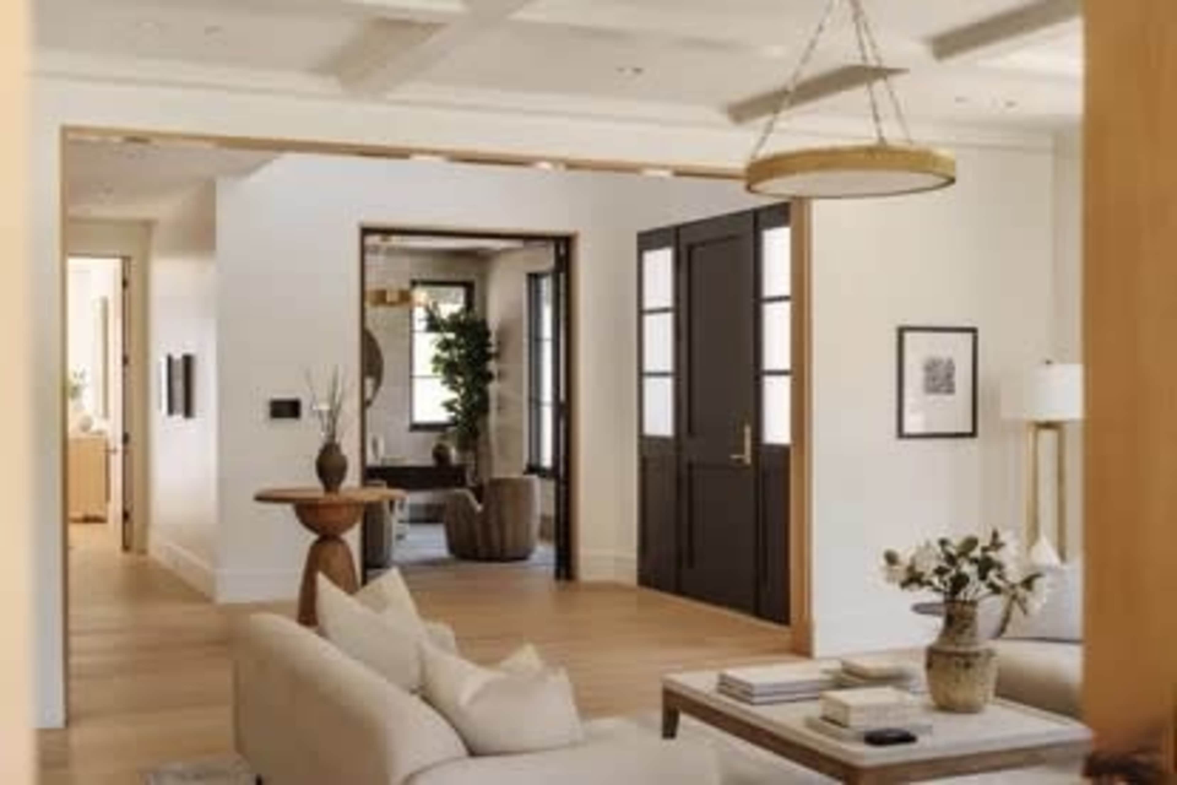 A bright, modern interior features a living room with a sofa, a coffee table, and an adjacent open doorway leading to another room.