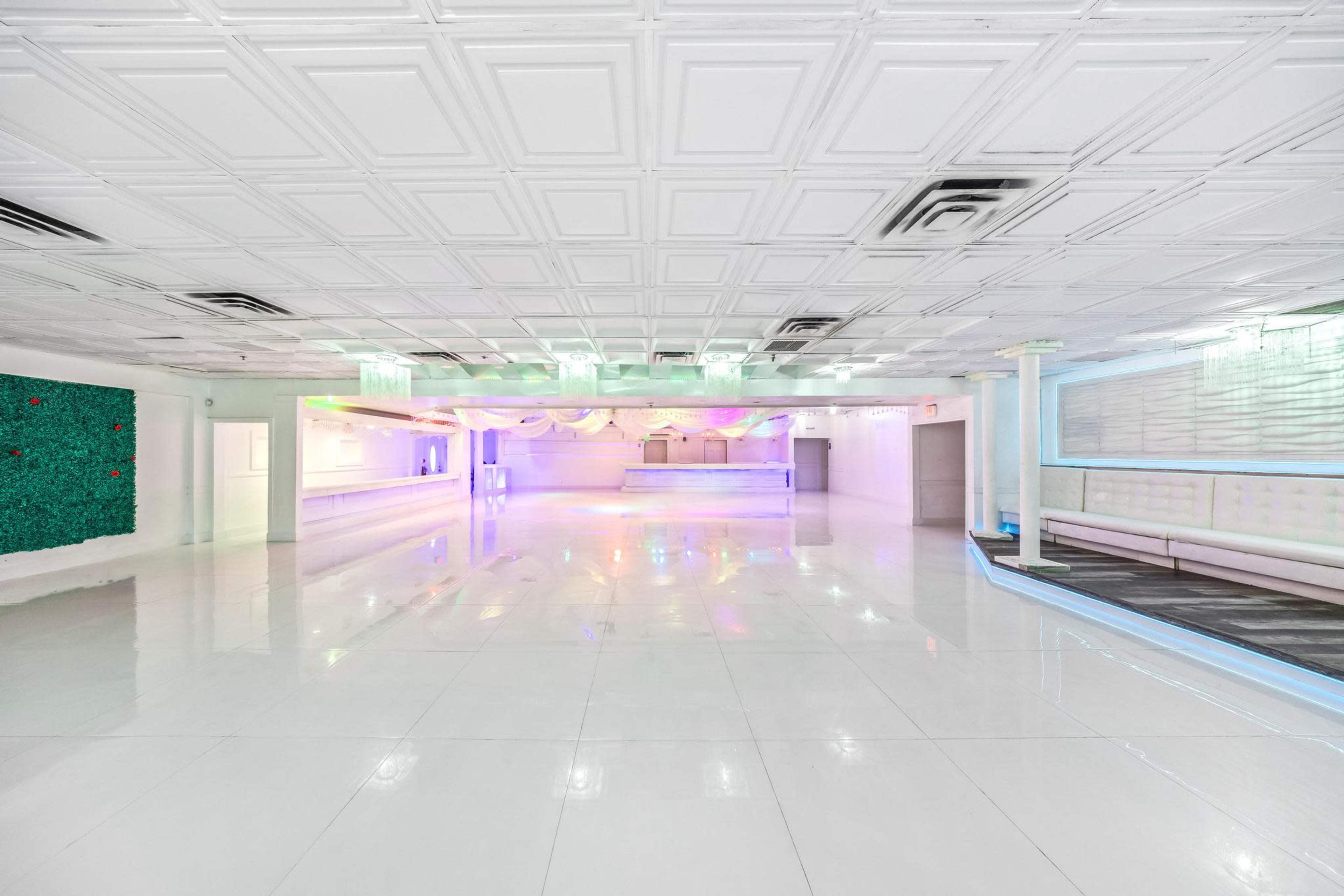 The image shows a spacious, well-lit event hall with white walls, a shiny floor, and colorful lighting accents.