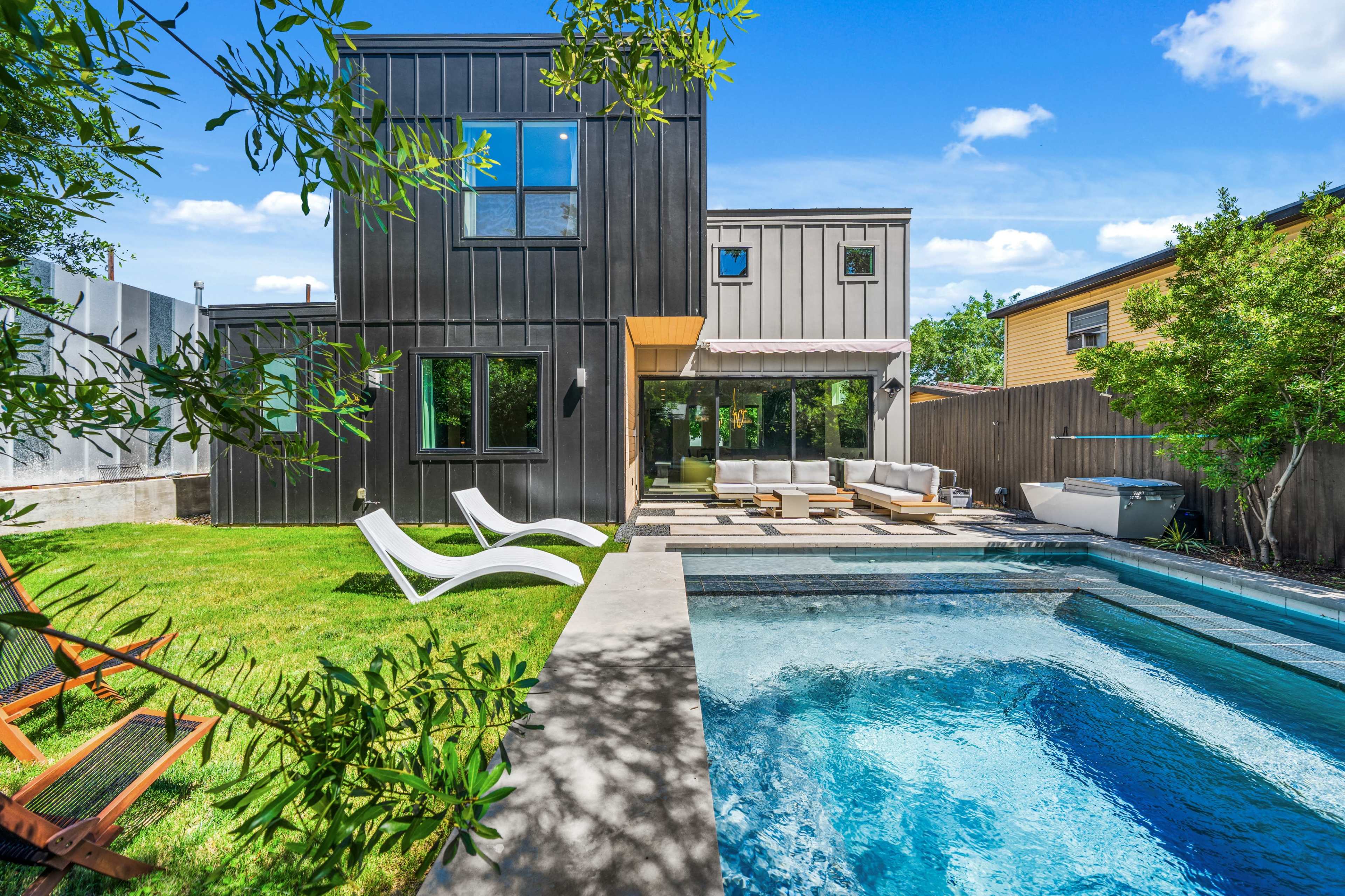 The image shows a modern two-story house with a pool and patio surrounded by green grass and trees.